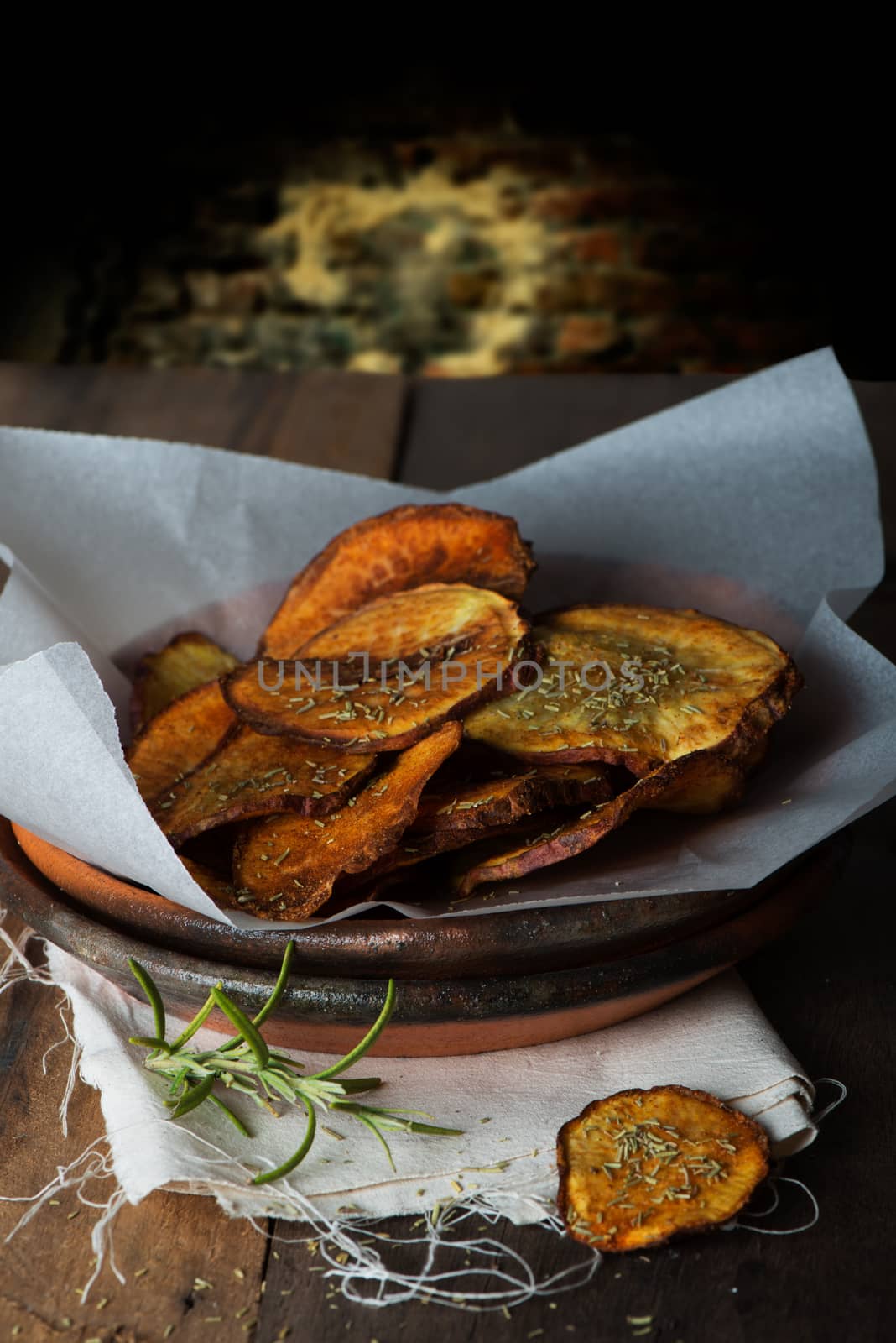 closeup of homemade sweet potatos chips on a wood table and a brick wall as background