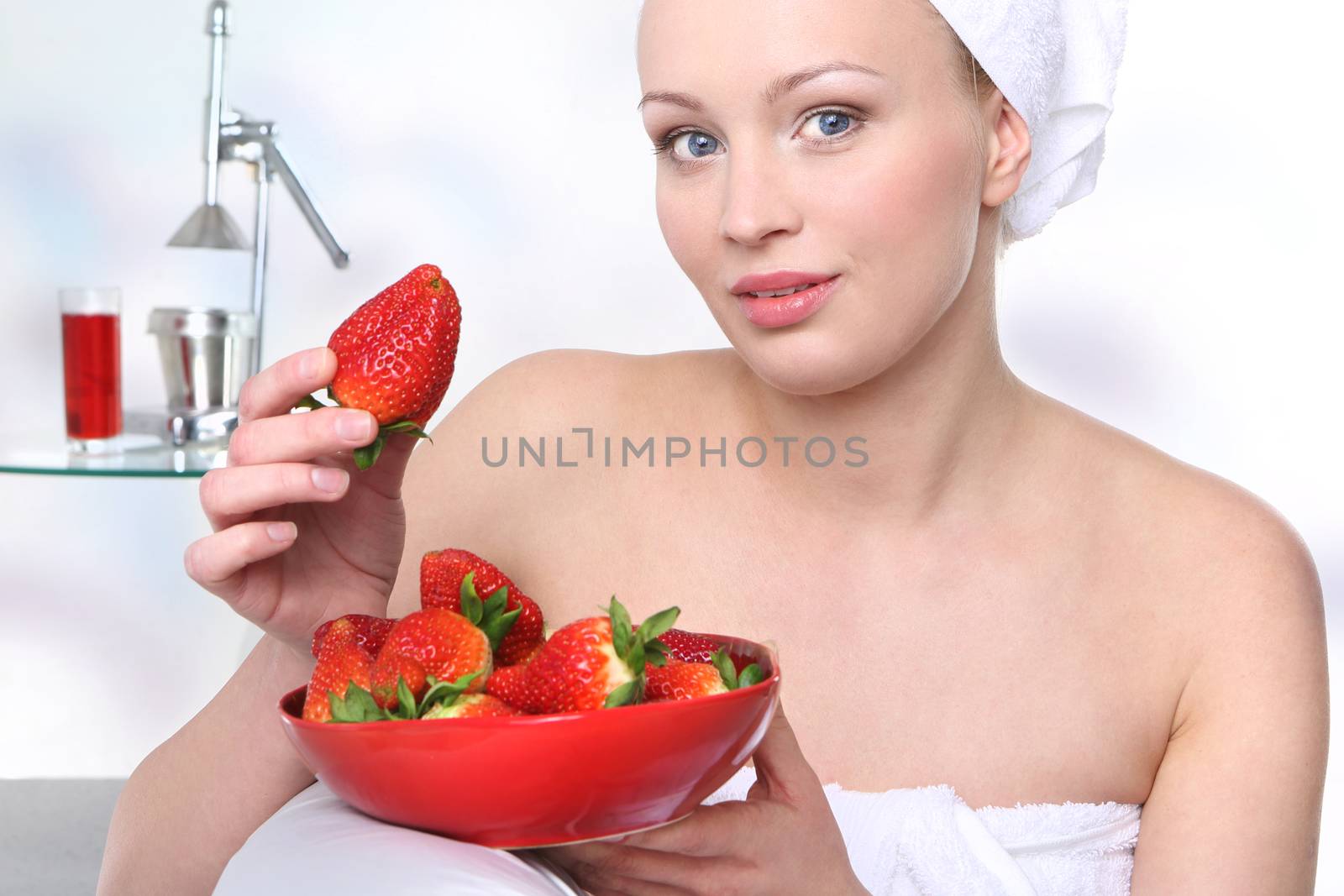 Attractive girl with a bowl of ripe strawberries relaxes in the living room.