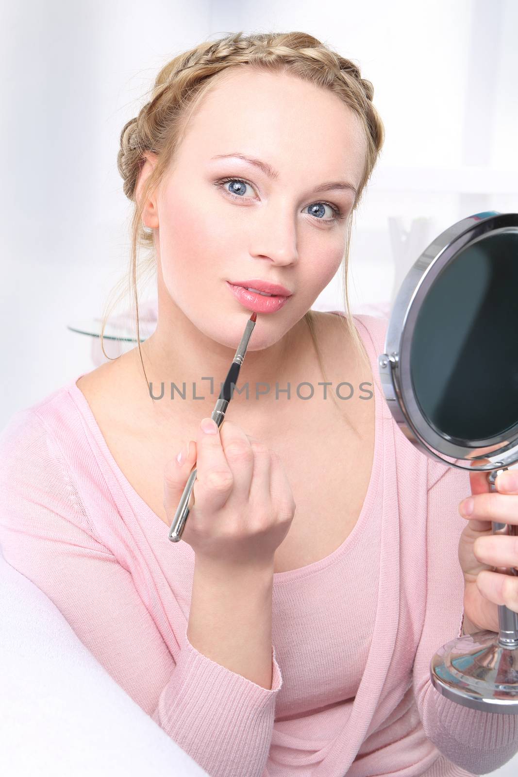 Woman in home arrangement paints lips looking through a mirror