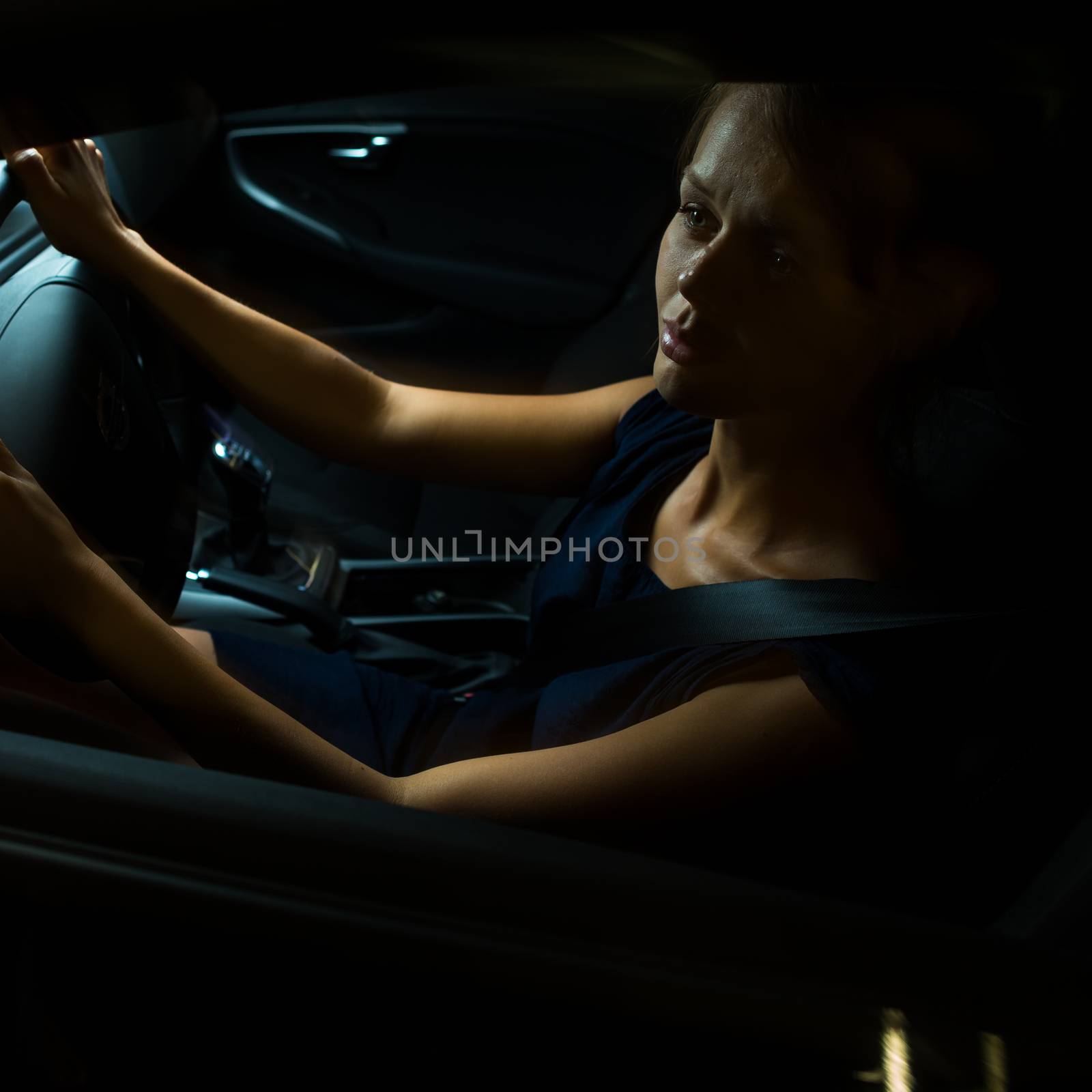 Driving a car at night - pretty, young woman driving her modern car at night, in a city (shallow DOF; color toned image)