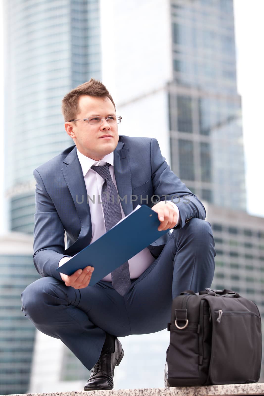 successful businessman sitting on his haunches and holding planning, against the background of office buildings