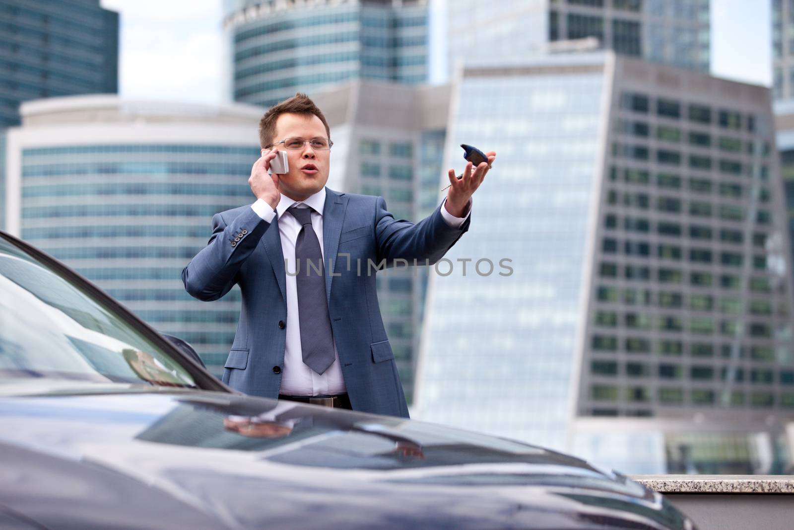 businessman on background of office near the car gives instructions over the phone and shows the hand