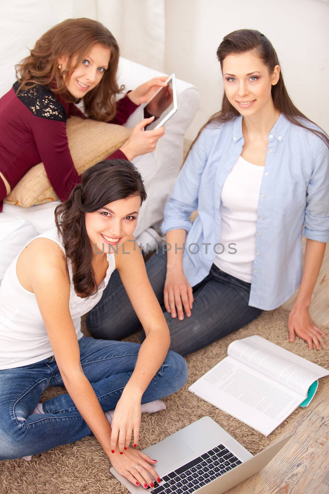 three young  women resting with notebook on floor near sofa, at campus