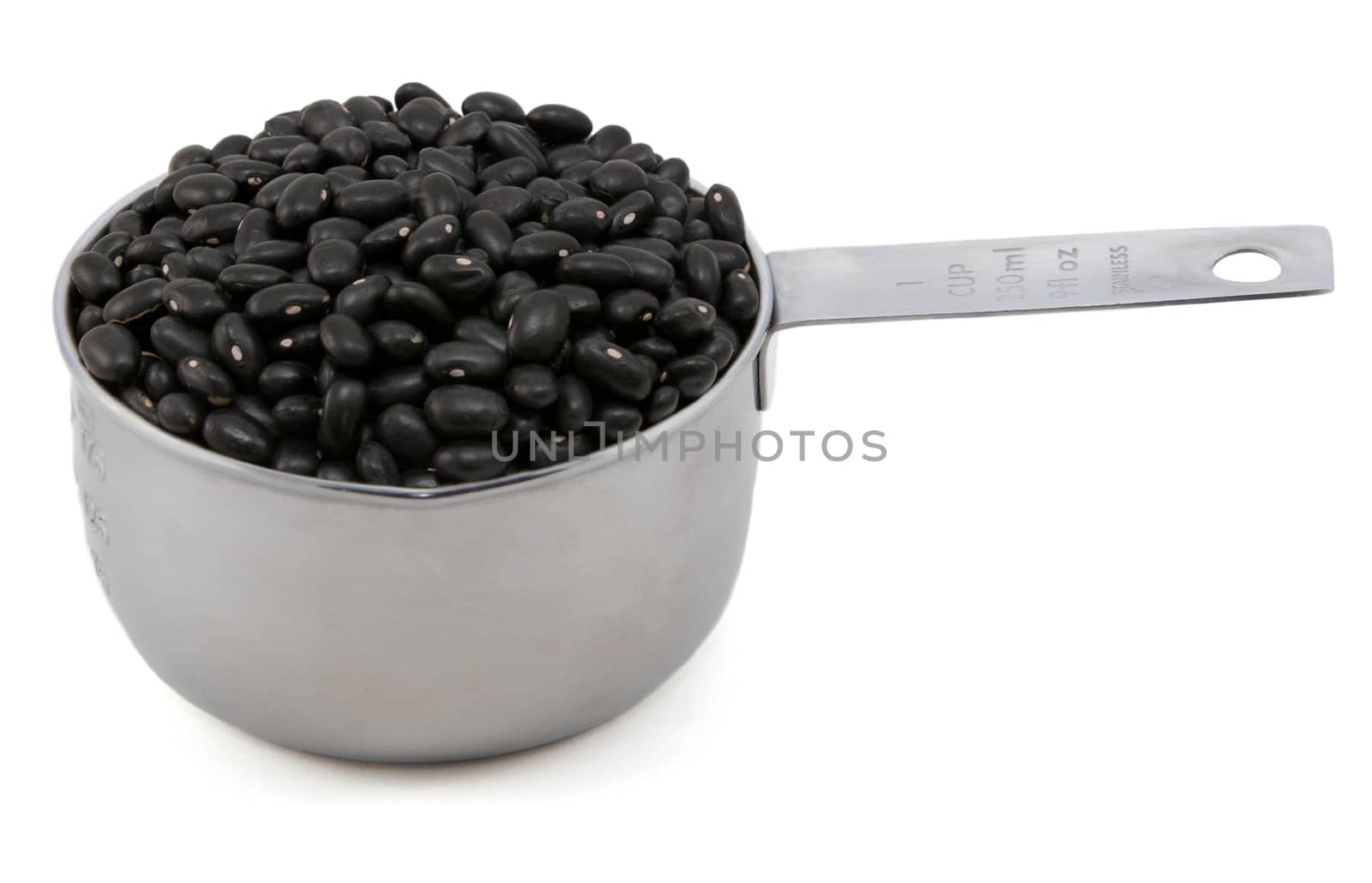 Black turtle beans in an American cup measure, isolated on a white background