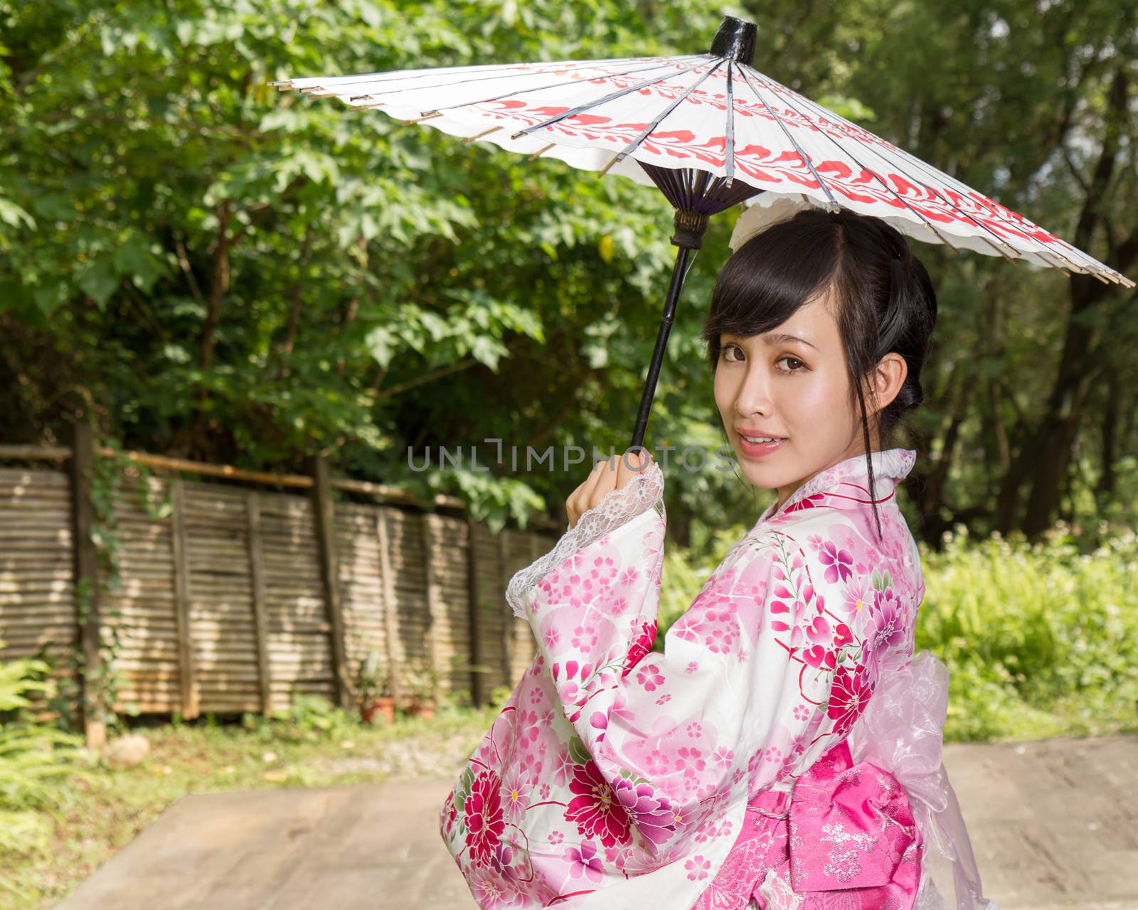 Asian woman in a kimono in a Japanese style garden holding an umbrella