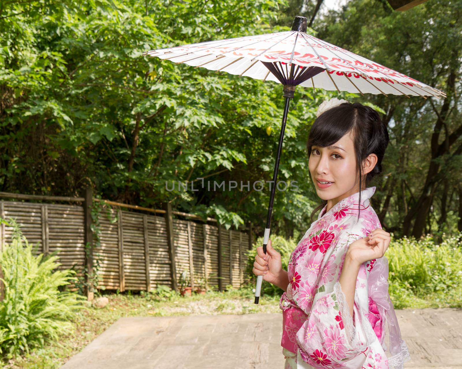 Asian woman wearing a kimono sitting in Japanese garden by imagesbykenny