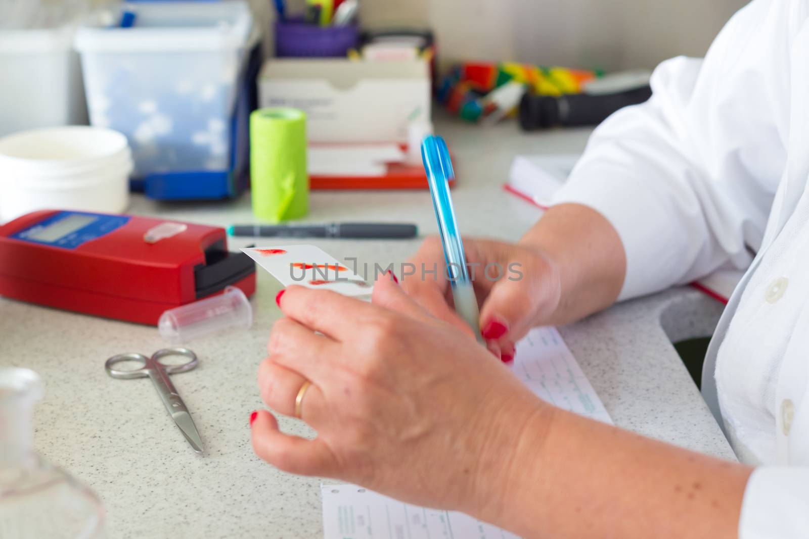 Medical doctor performing a quick blood group determination by using blood type testing kit with anti A and B antibodies on a white card.