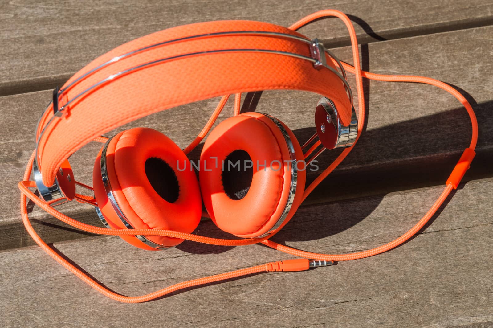 Vibrant orange wired headphones on the wooden bench