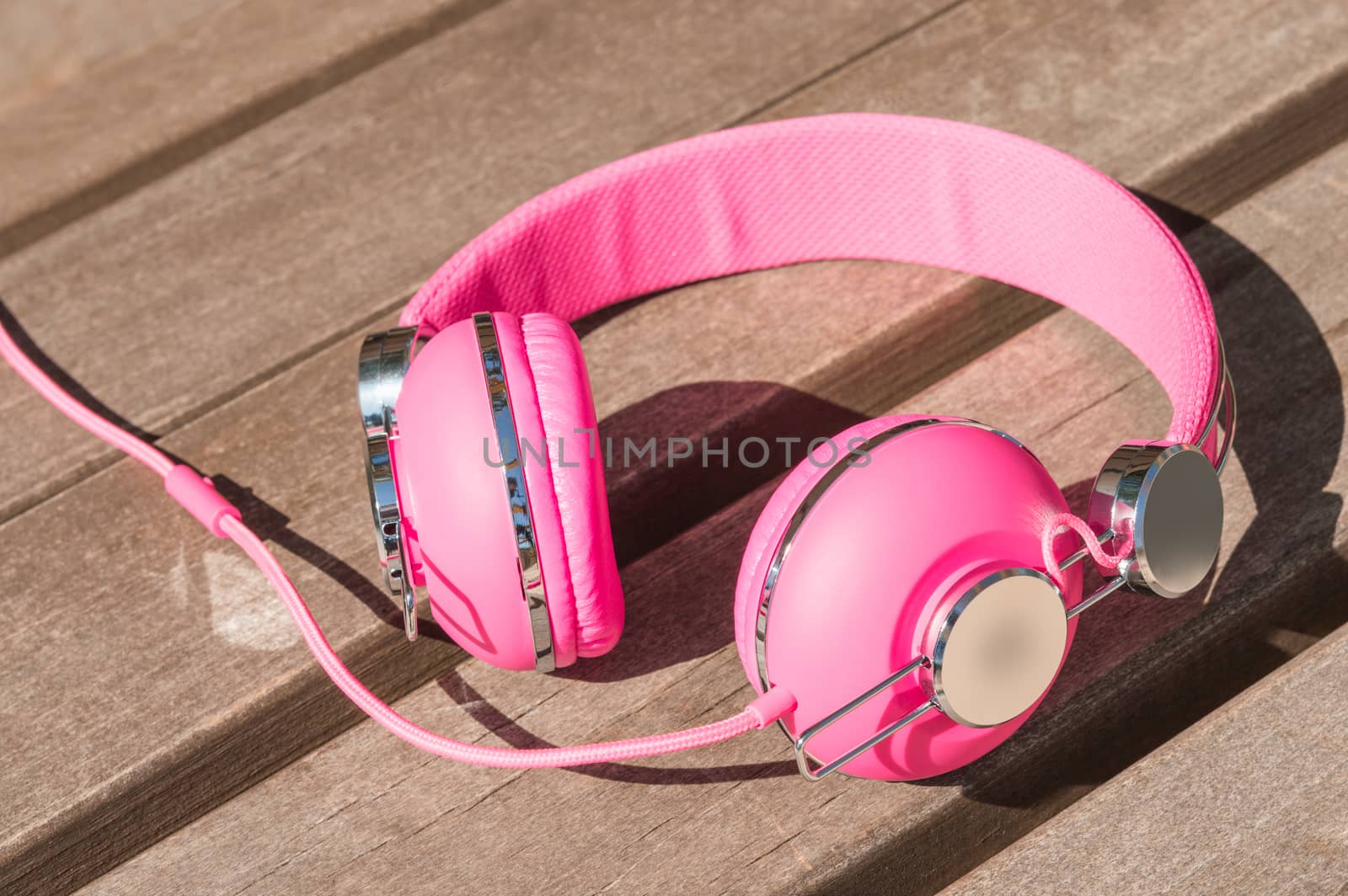 Vivid pink wired headphones on wooden bench in park