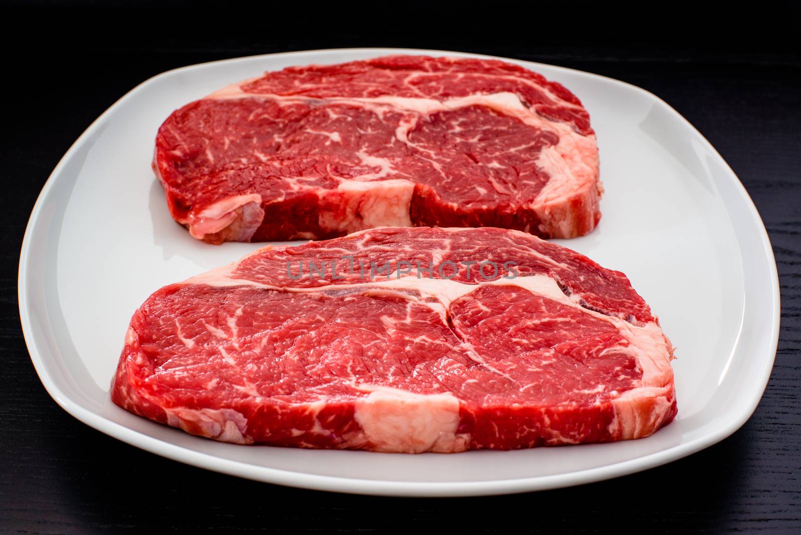 two delicious entrecote steaks on a white plate with dark wooden table in the background