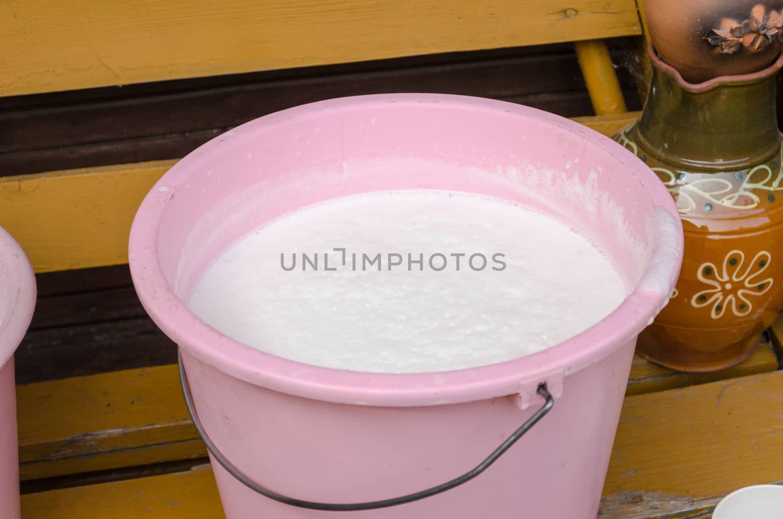 pink plastic bucket full of fresh cow milk on wooden yellow bench