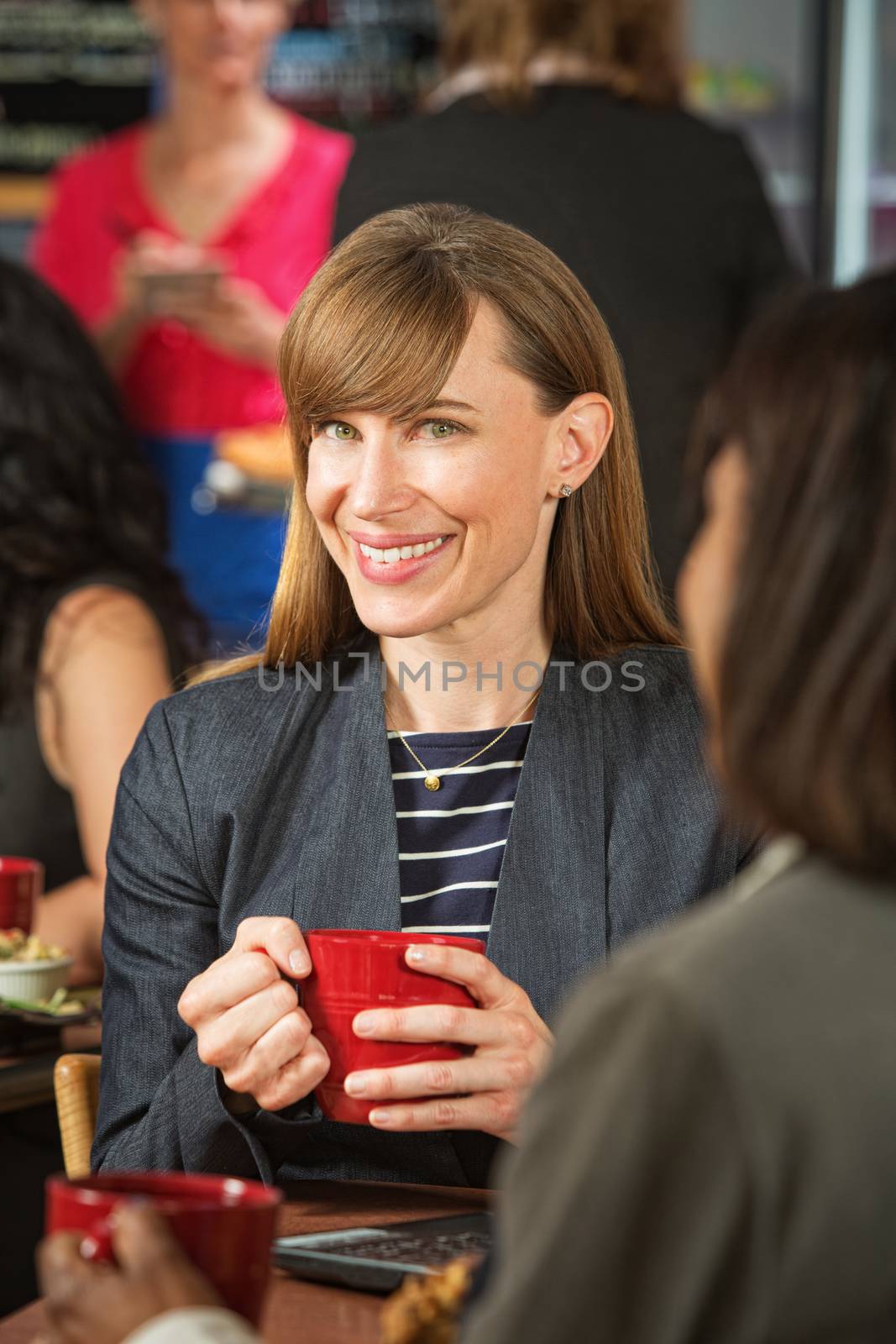 Cheerful business woman with red mug and friend in cafe