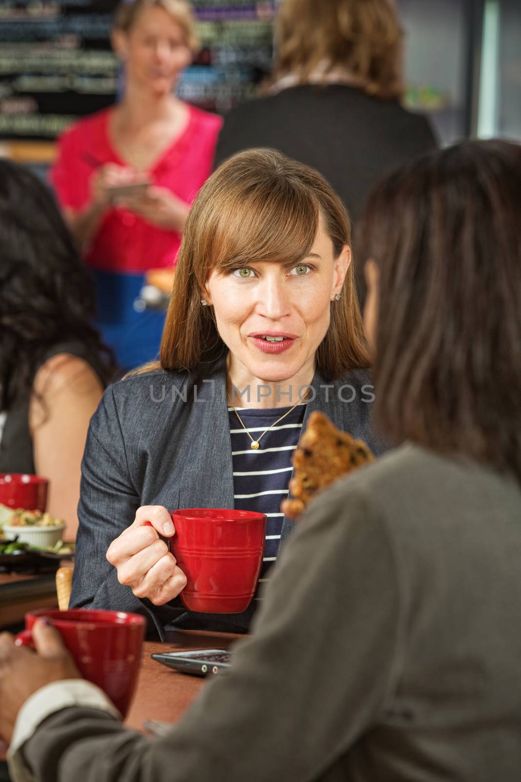 Excited woman holding cookie with friend in cafe