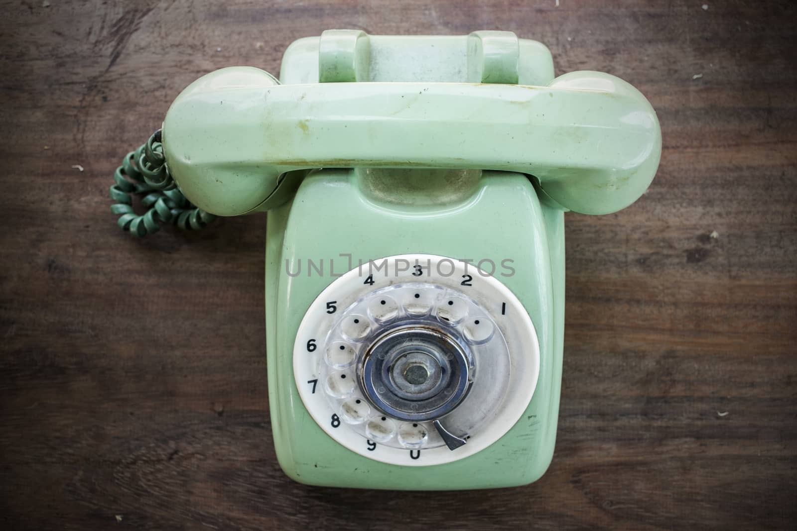 Green vintage telephone on brown wood desk background by 2nix