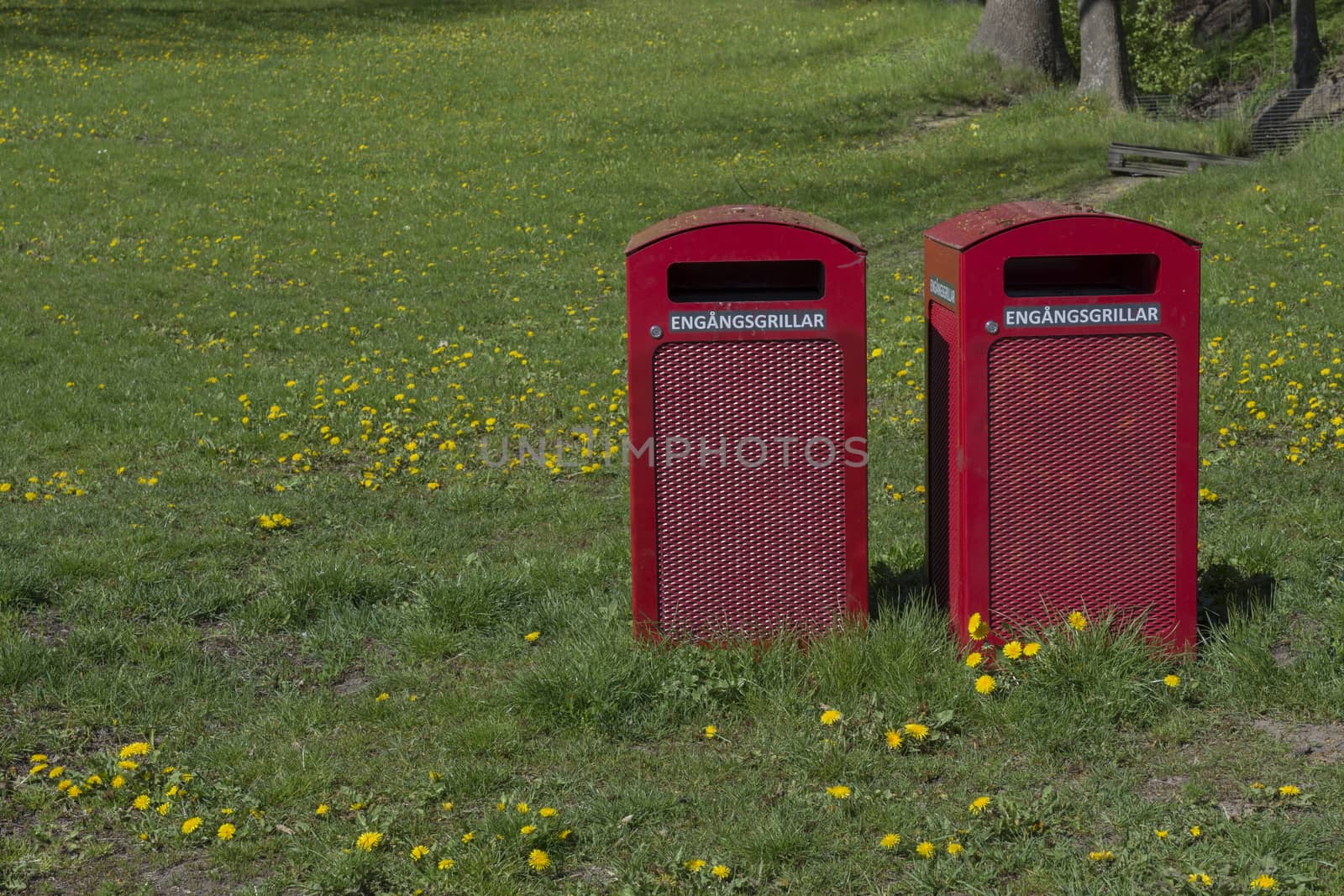 Two red garbage bins with text 'engangsgrillar' for disposable barbecue items in a park, Stockholm, Sweden in May.