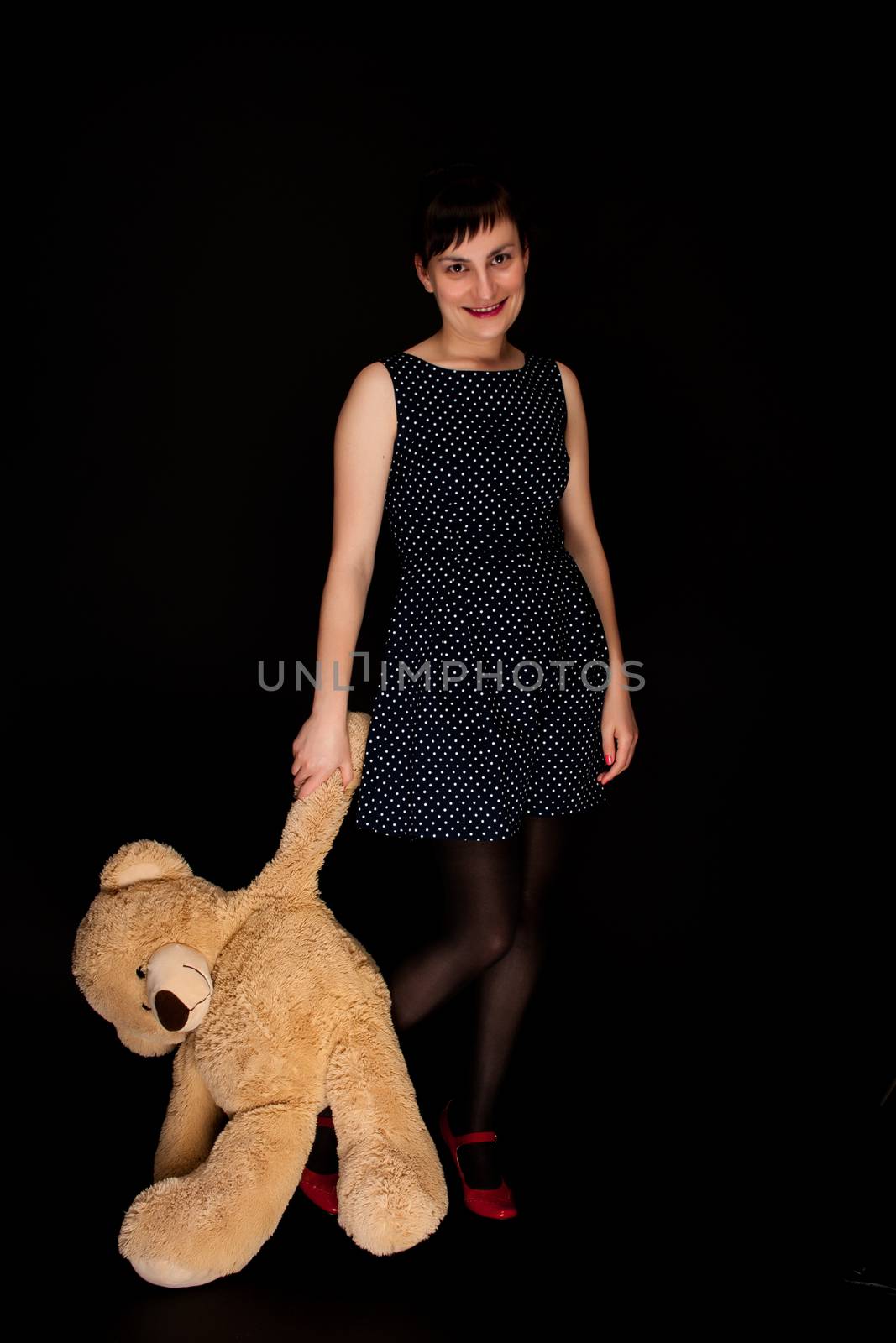 stylish expressive woman with red shoes on black background with teddy bear