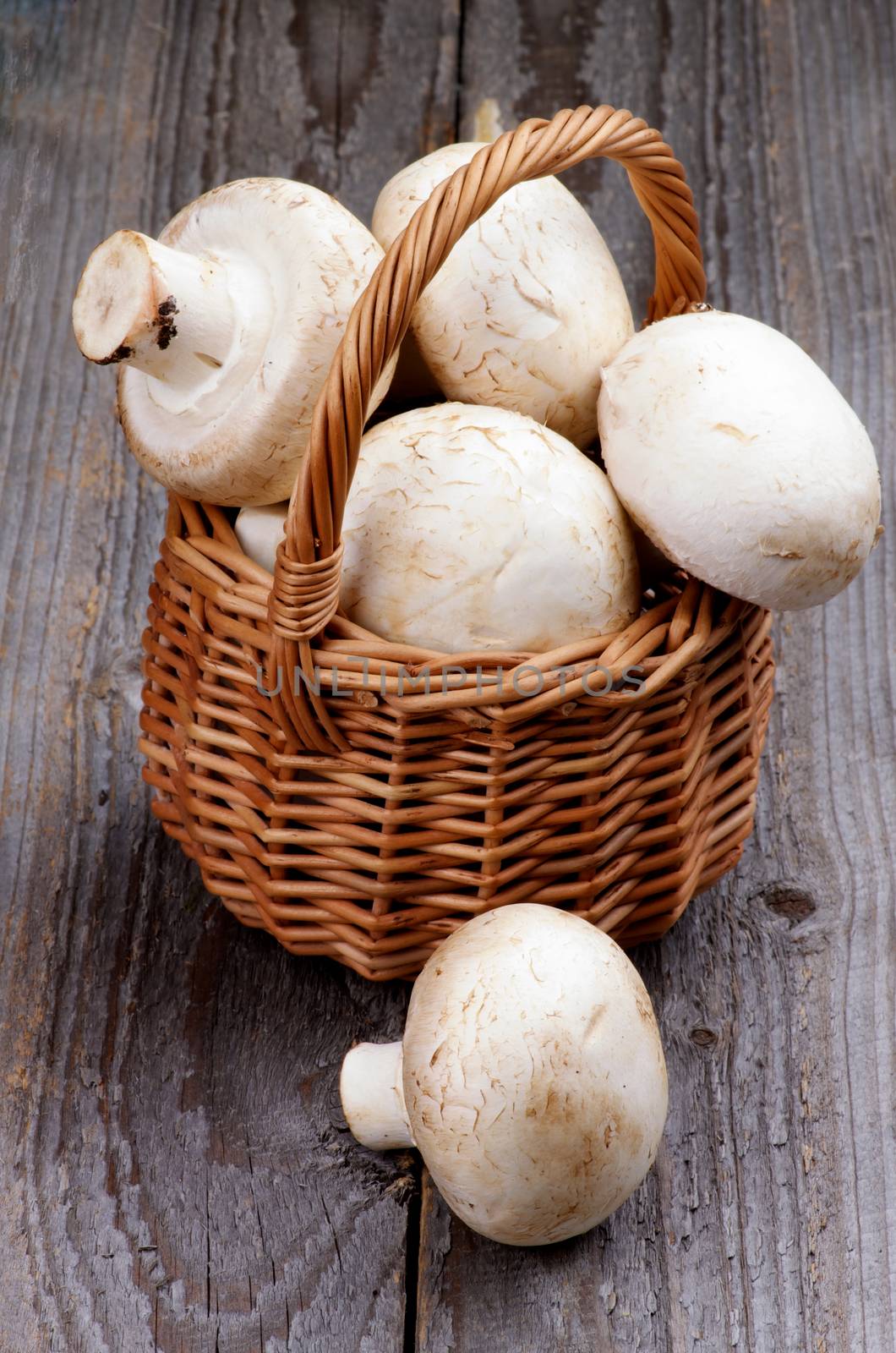 Big Raw Champignons in Wicker Basket isolated on Rustic Wooden background
