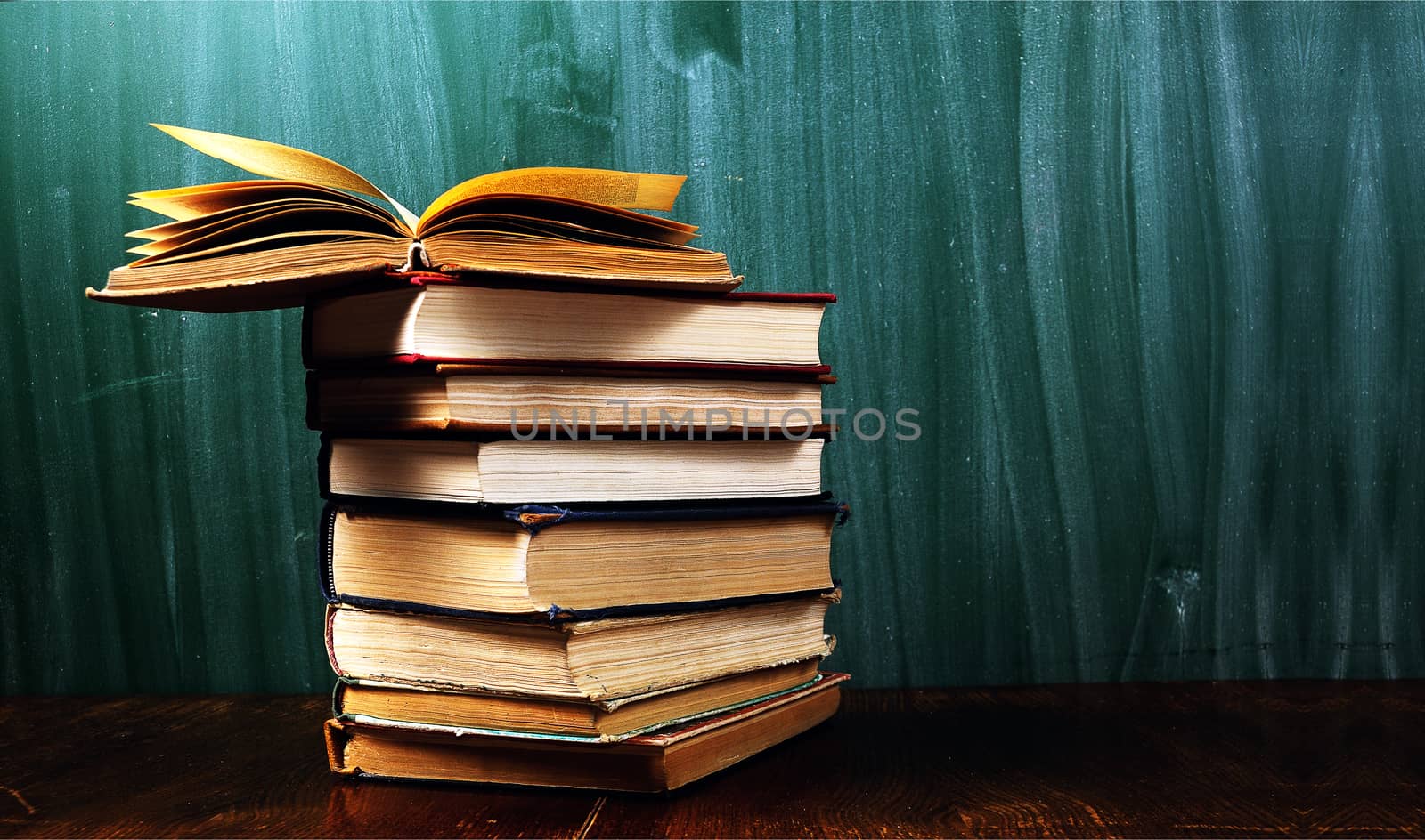 stack of books in front of  blank  green  blackboard .Warm tones.