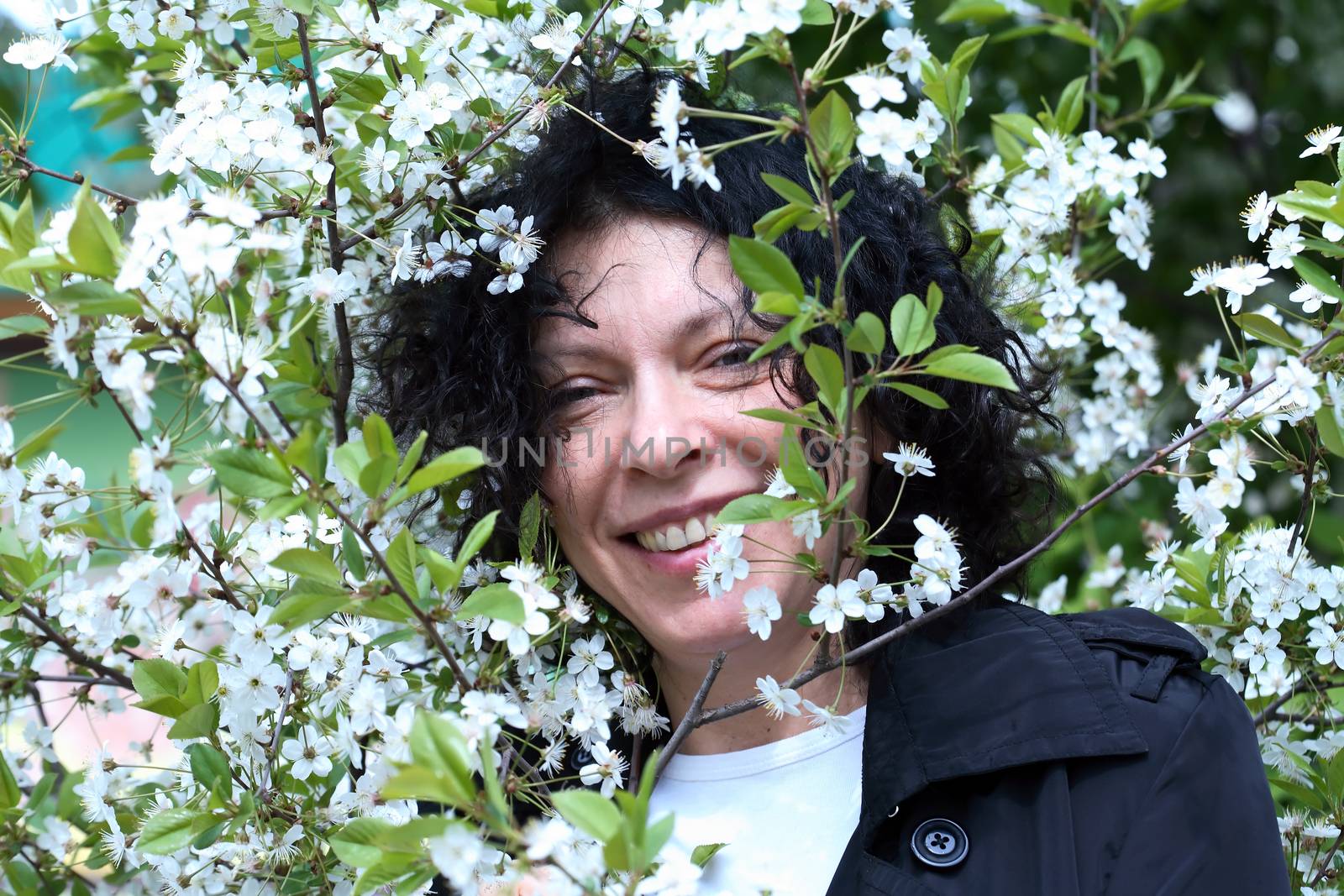 Portrait of smiling mature woman between twigs of blooming spring tree with white flowers