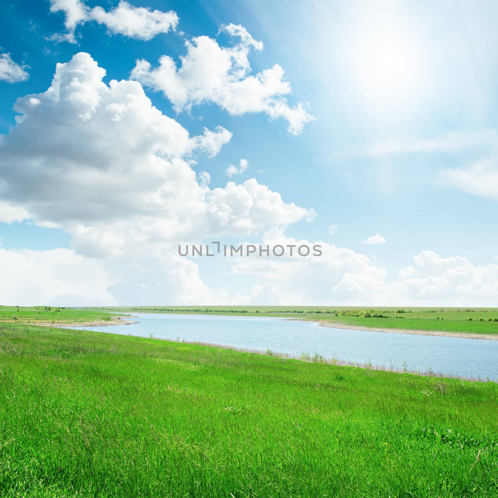 sun in cloudy sky over river with green sides