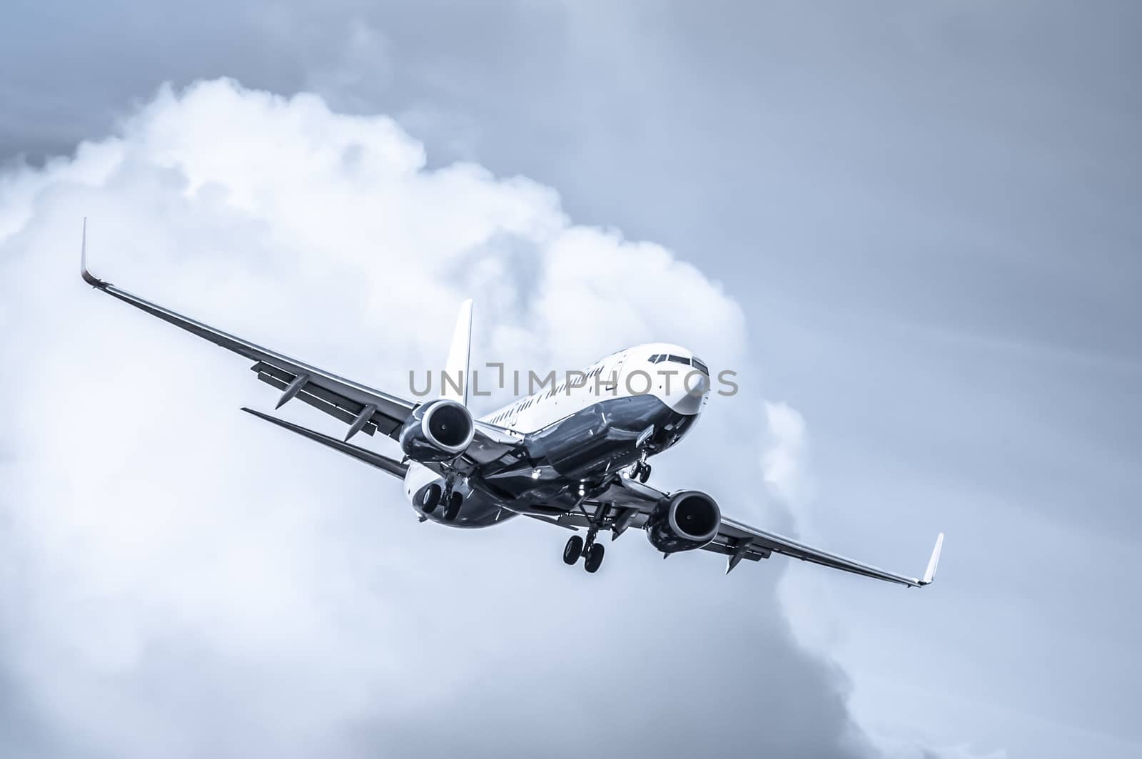 cool toned passenger jet on landing approach through a cloudy sky