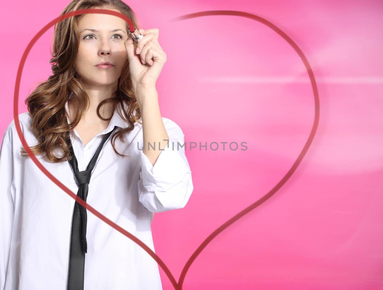Woman painting lipstick heart on glass standing on a pink background