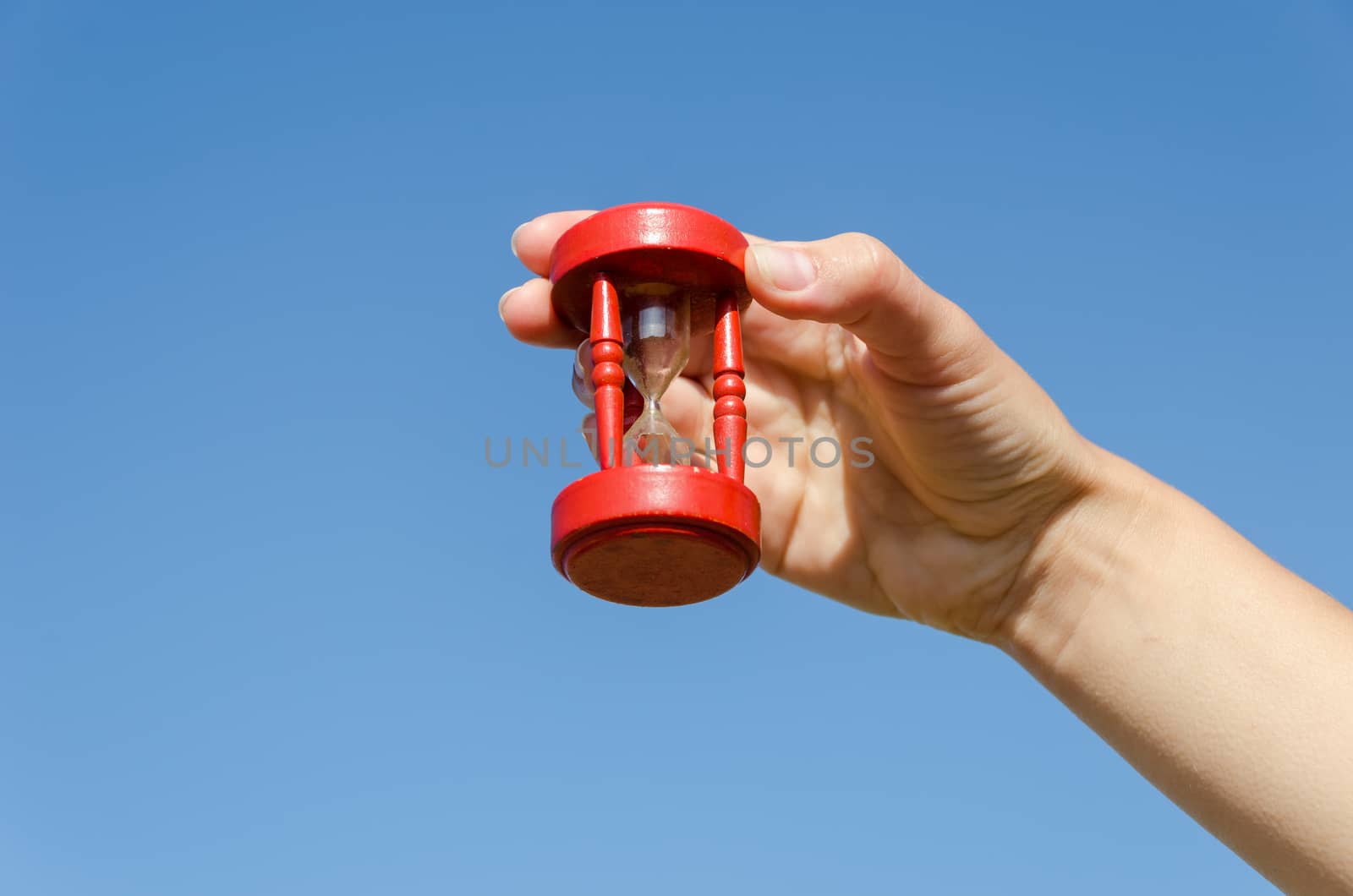 red wooden old hourglass in female hand on blue sky background