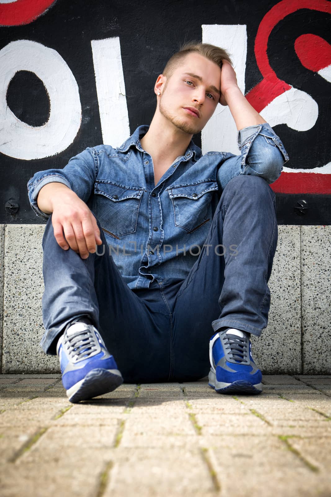 Attractive young blond man against colorful graffiti wall, wearing denim shirt by artofphoto