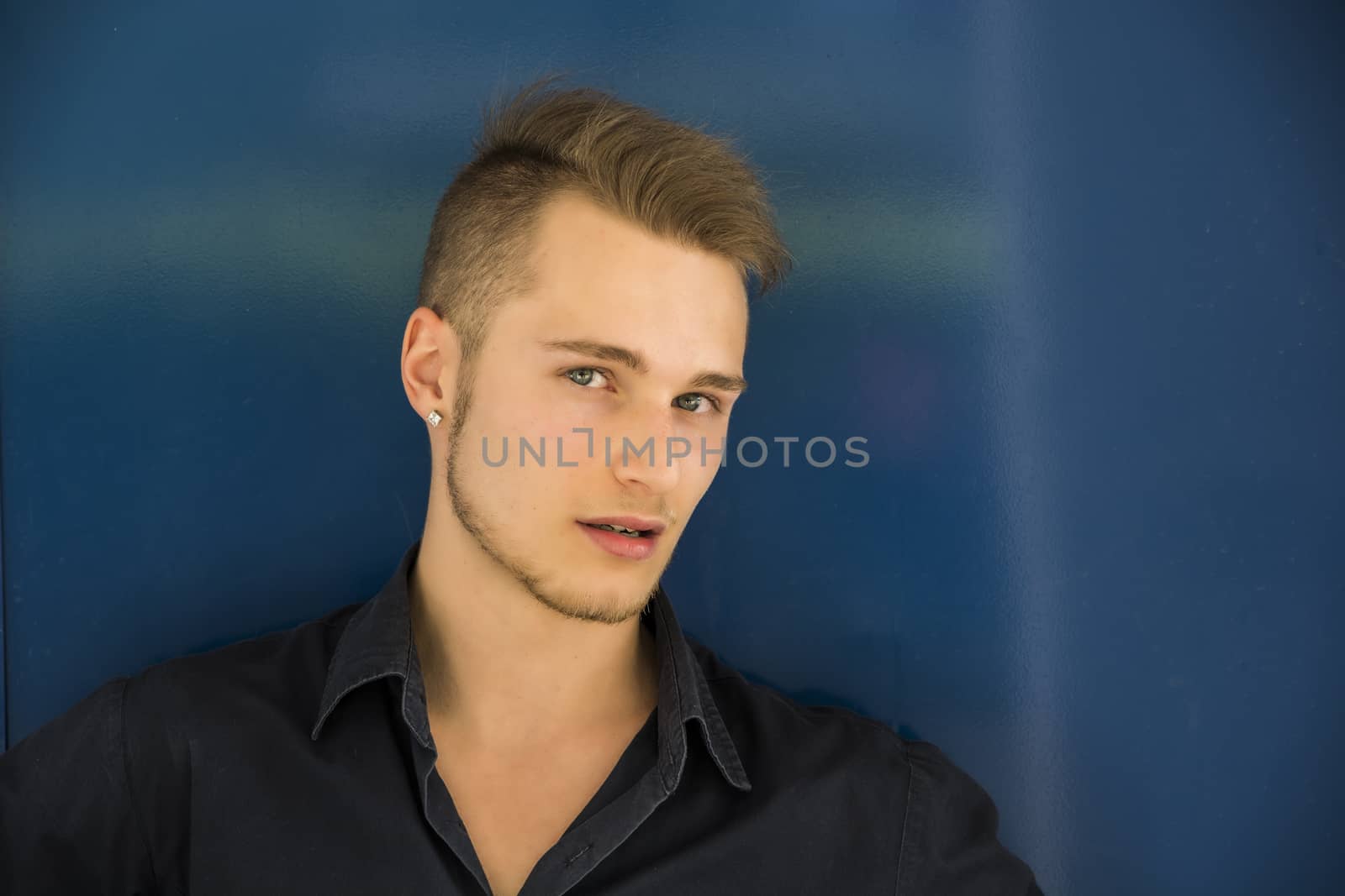 Handsome blond young man against metal blue wall, looking at camera