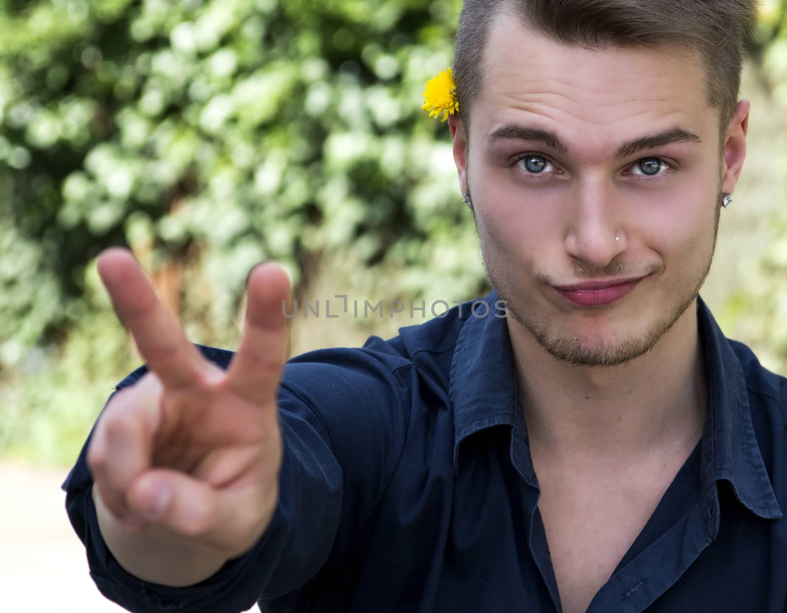 Handsome blond young man outdoors in nature doing peace sign with fingers
