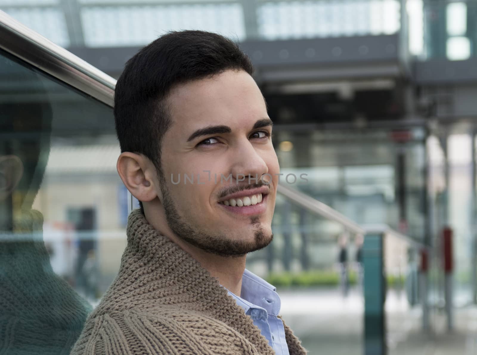 Handsome young man in public place (station, airport) smiling at camera