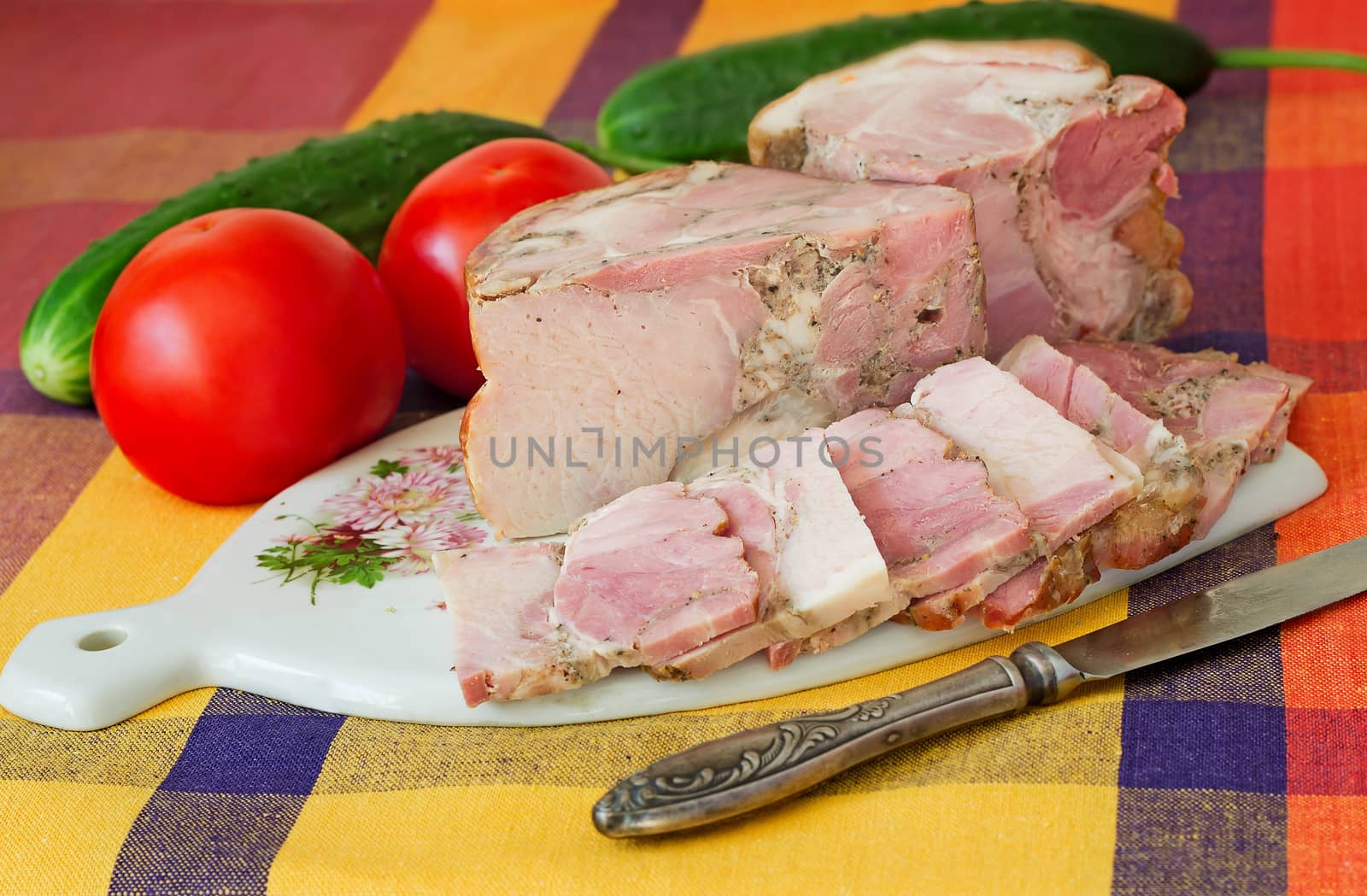 The big appetizing piece of smoked pork with vegetables is located on a table on a white plate.