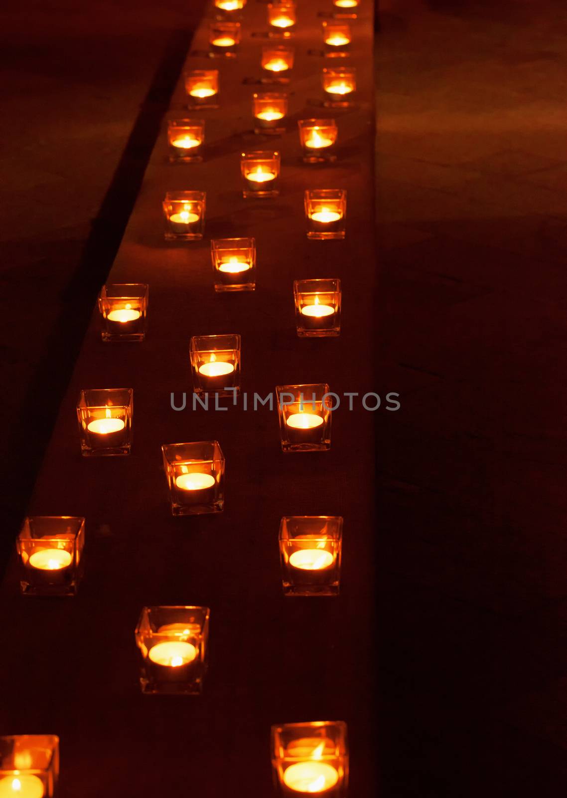 A long row of small candles in square glasses