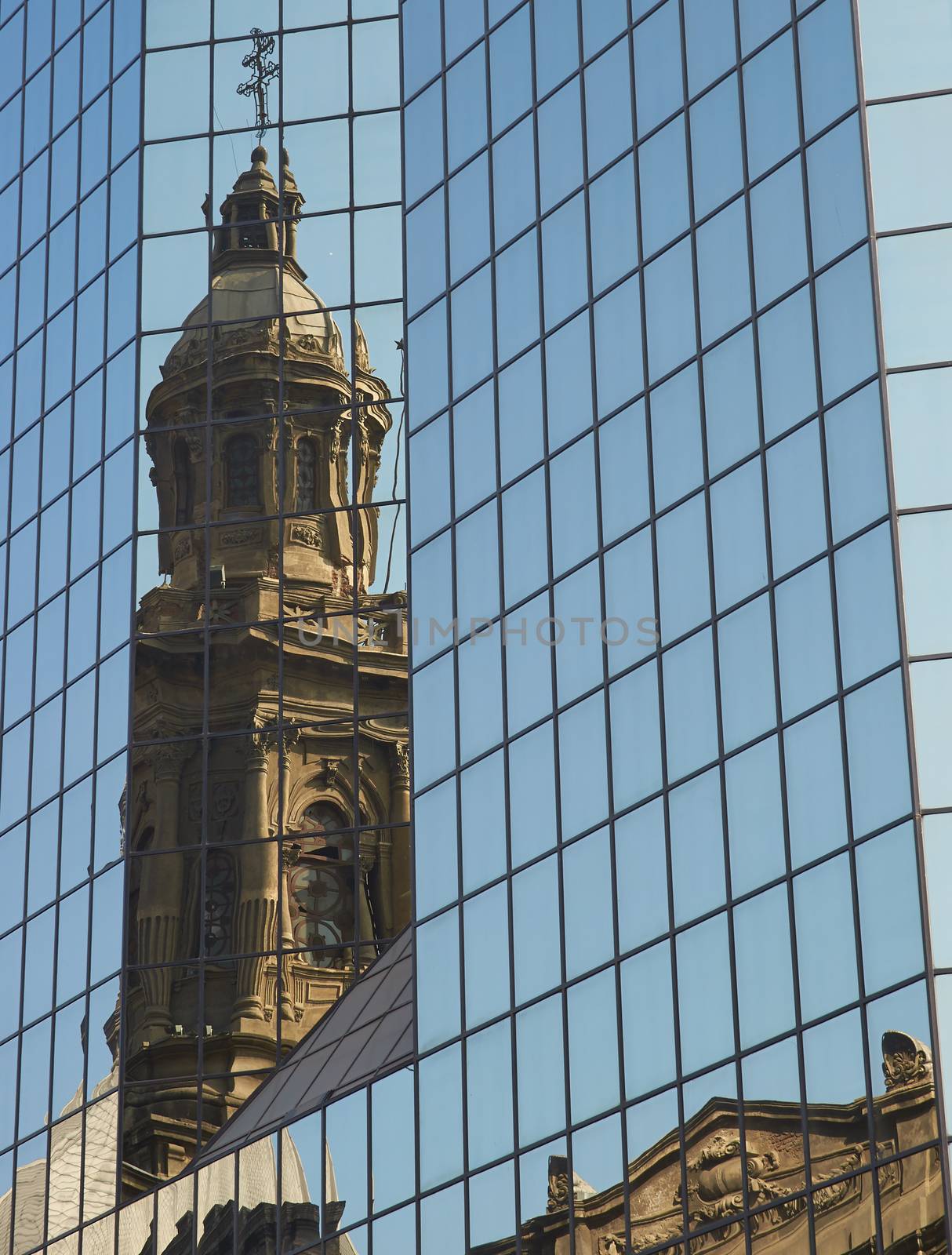Tower of the historic Catedral Metropolitana reflected in the glass of a modern office building in the Plaza de Armas in Santiago, Chile