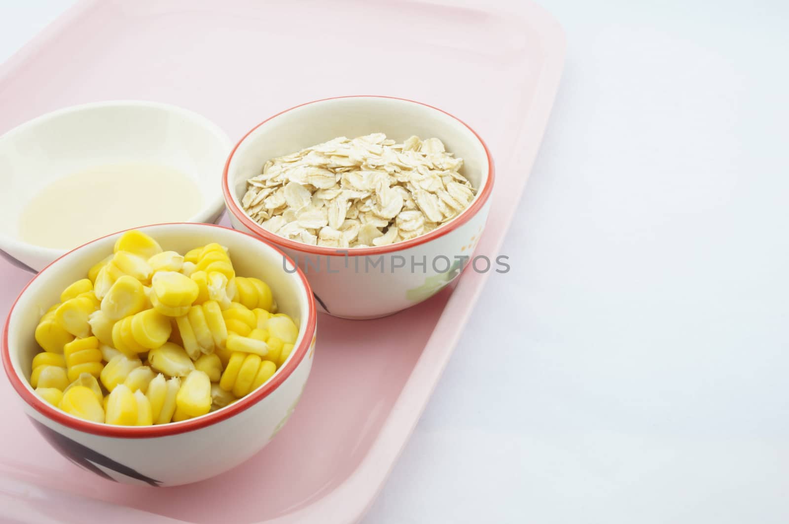 Corn, oats and sweetened condensed milk placed on pink tray with white background.