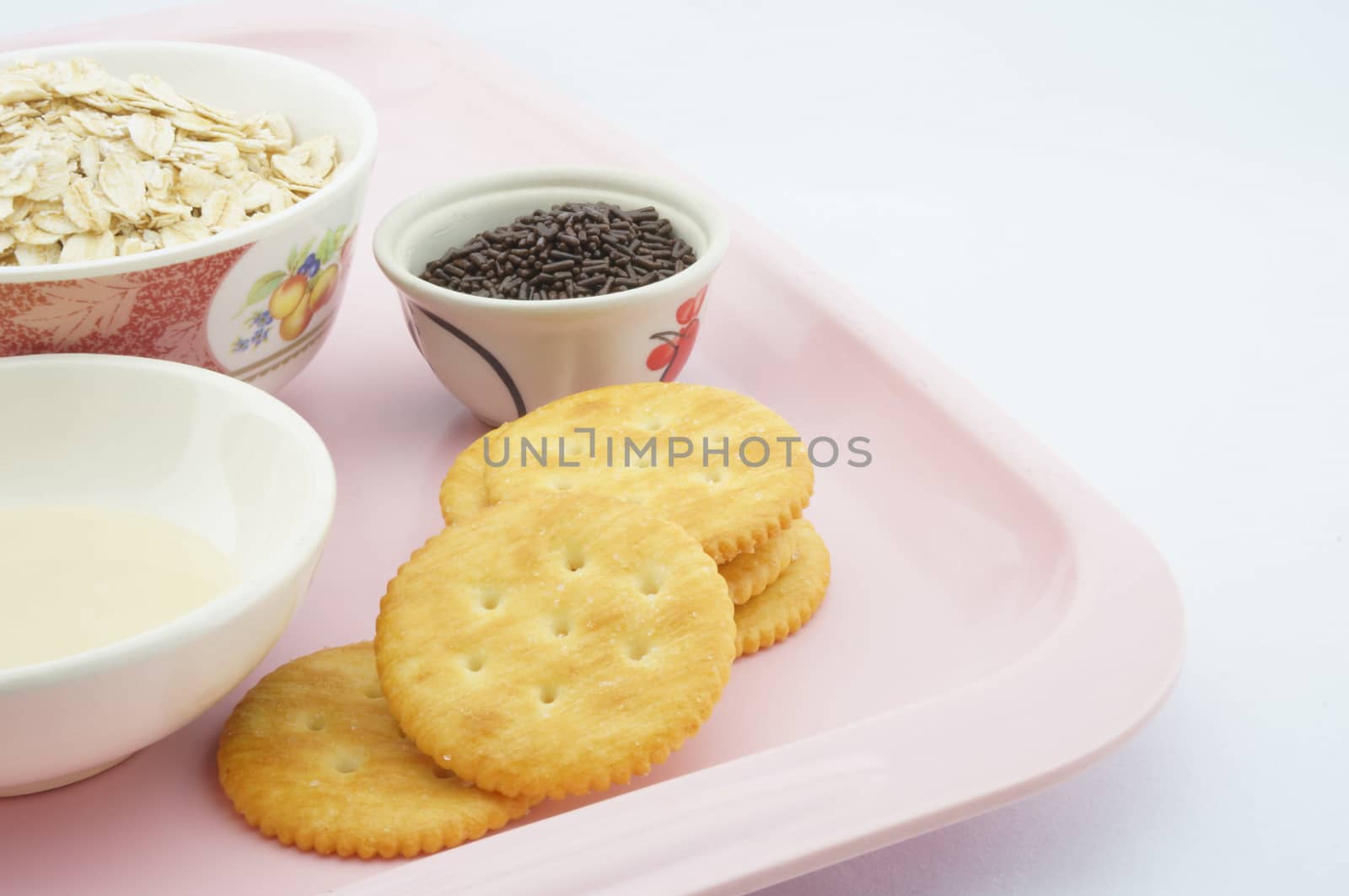 Cracker, oat, chocolate and  sweetened condensed milk placed on a pink plate.
