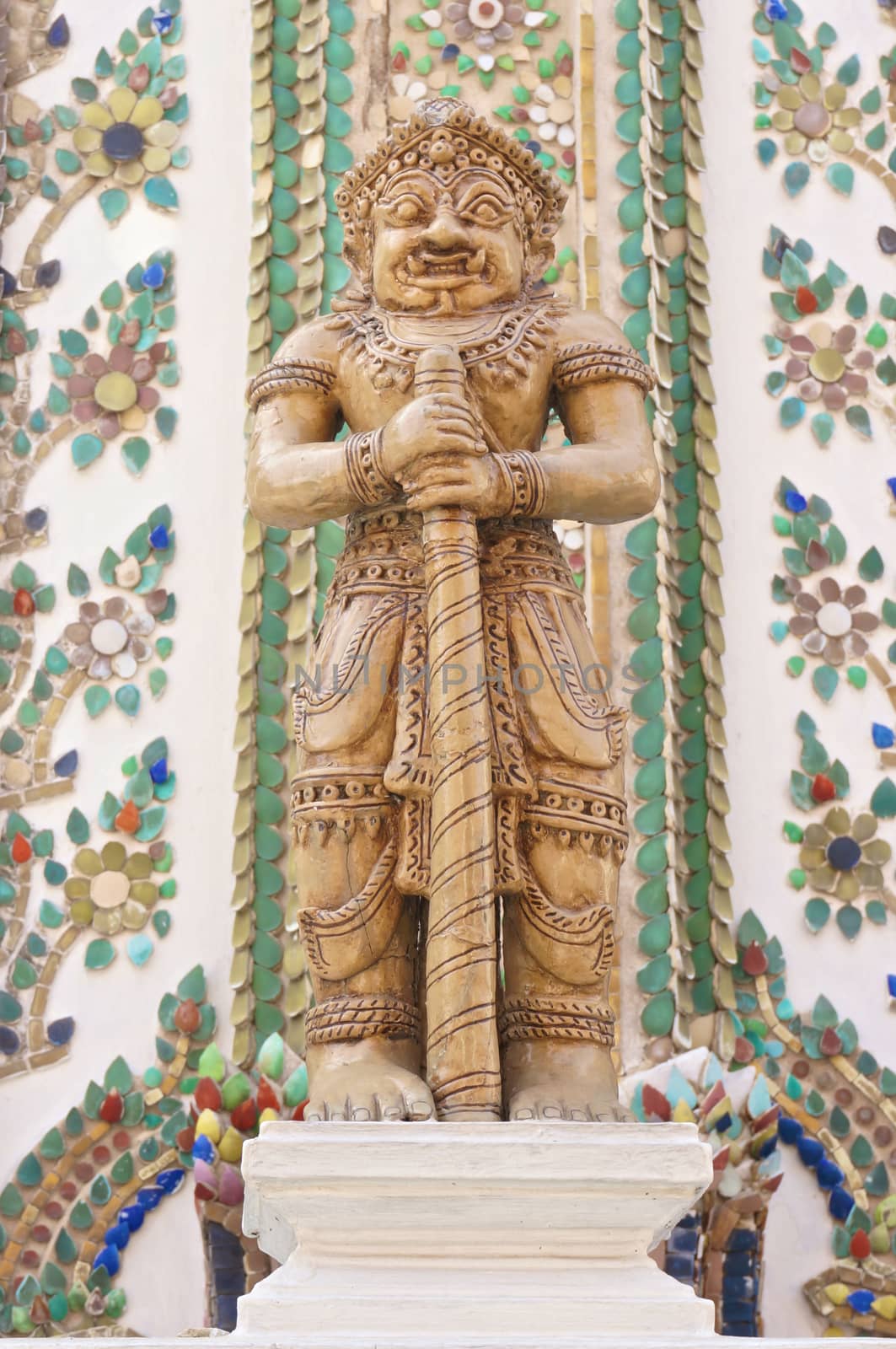 A brown giant statue hold baton stand on base at Wat Pho