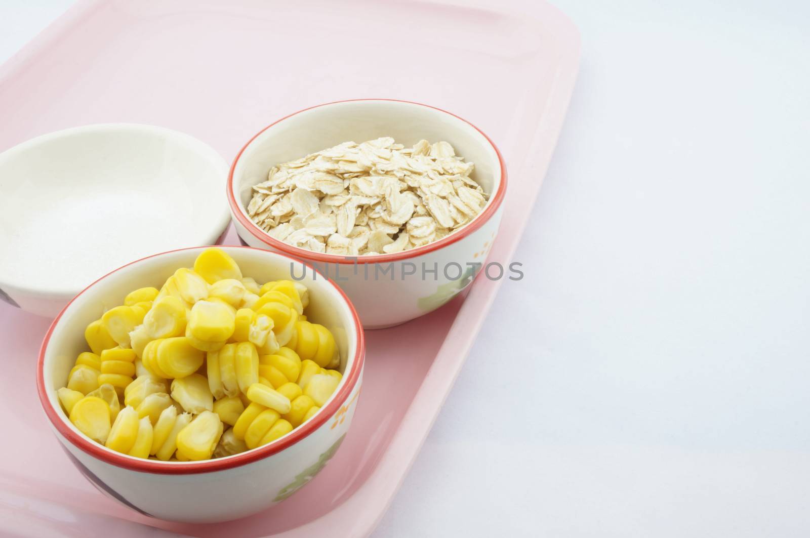 Corn, oats and sugar placed on pink tray with white background.