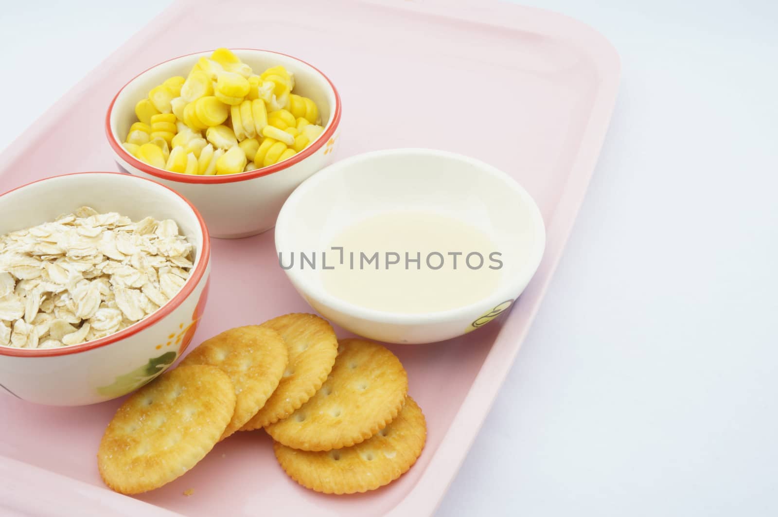 Corn, oats, cracker and sweetened condensed milk placed on pink tray with white background.