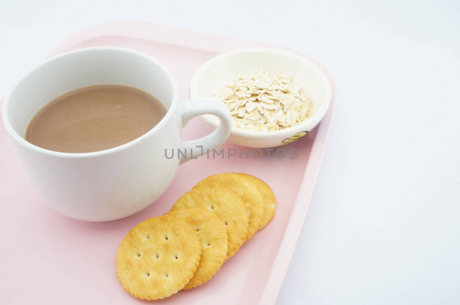 Cup of coco, oats in a small bowl and cracker placed on pink tray with white background.