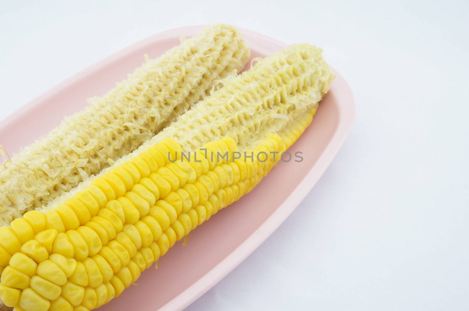 Corn eating and cob placed on pink trays with white background.