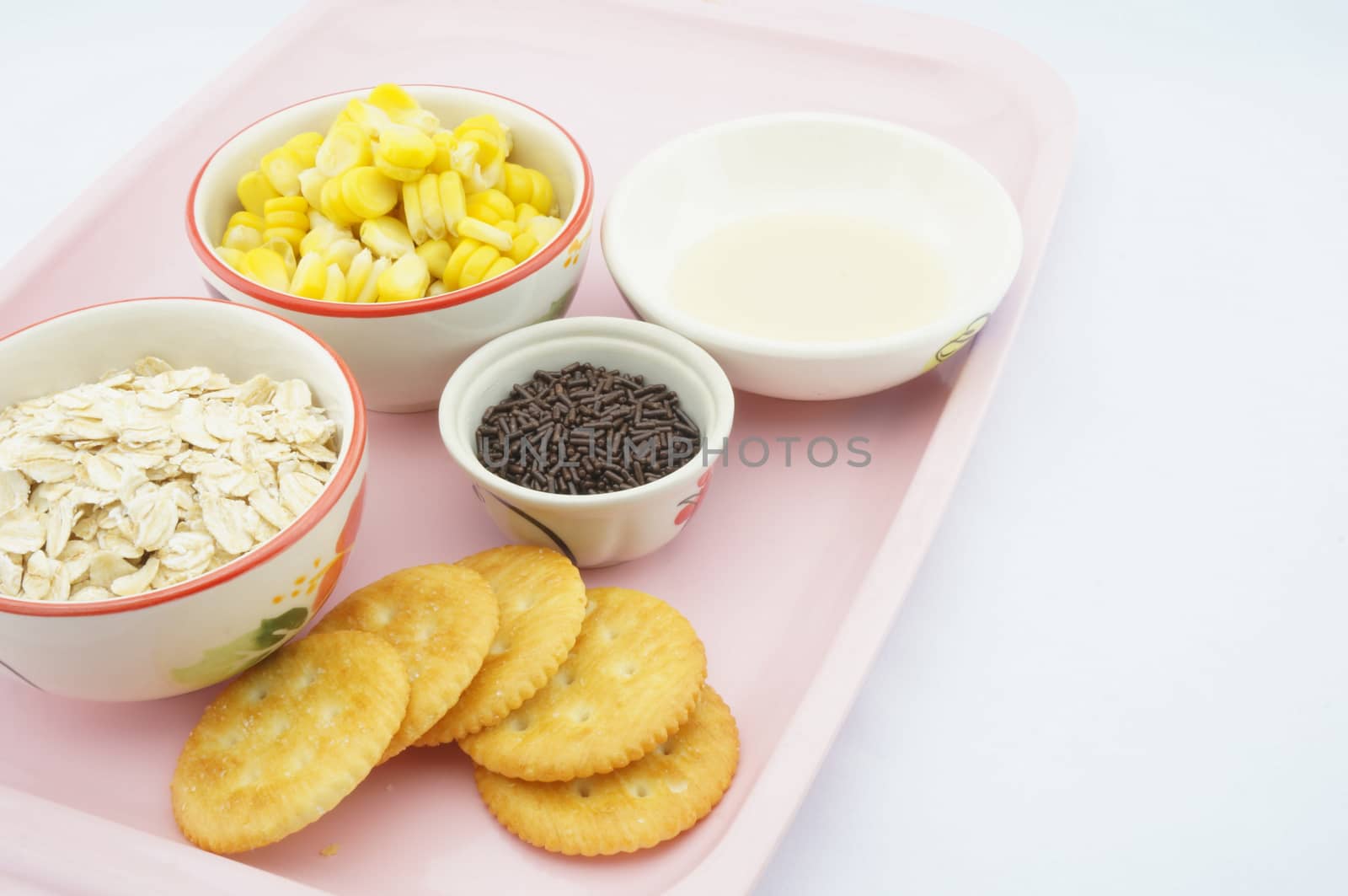 Corn, oats, chocolate, cracker and sweetened condensed milk placed on pink tray with white background.