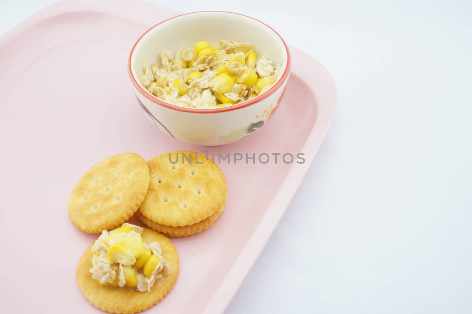 Mix corn, oats and sweetened condensed milk put on cracker placed on pink tray with white background.