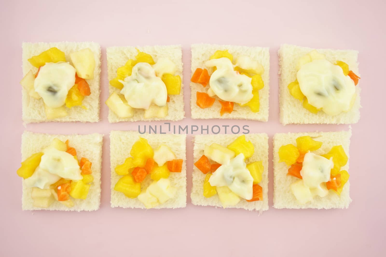 Carrot, Mango, apple and cucumber sliced put on small bread with cream salad in row on pink tray.