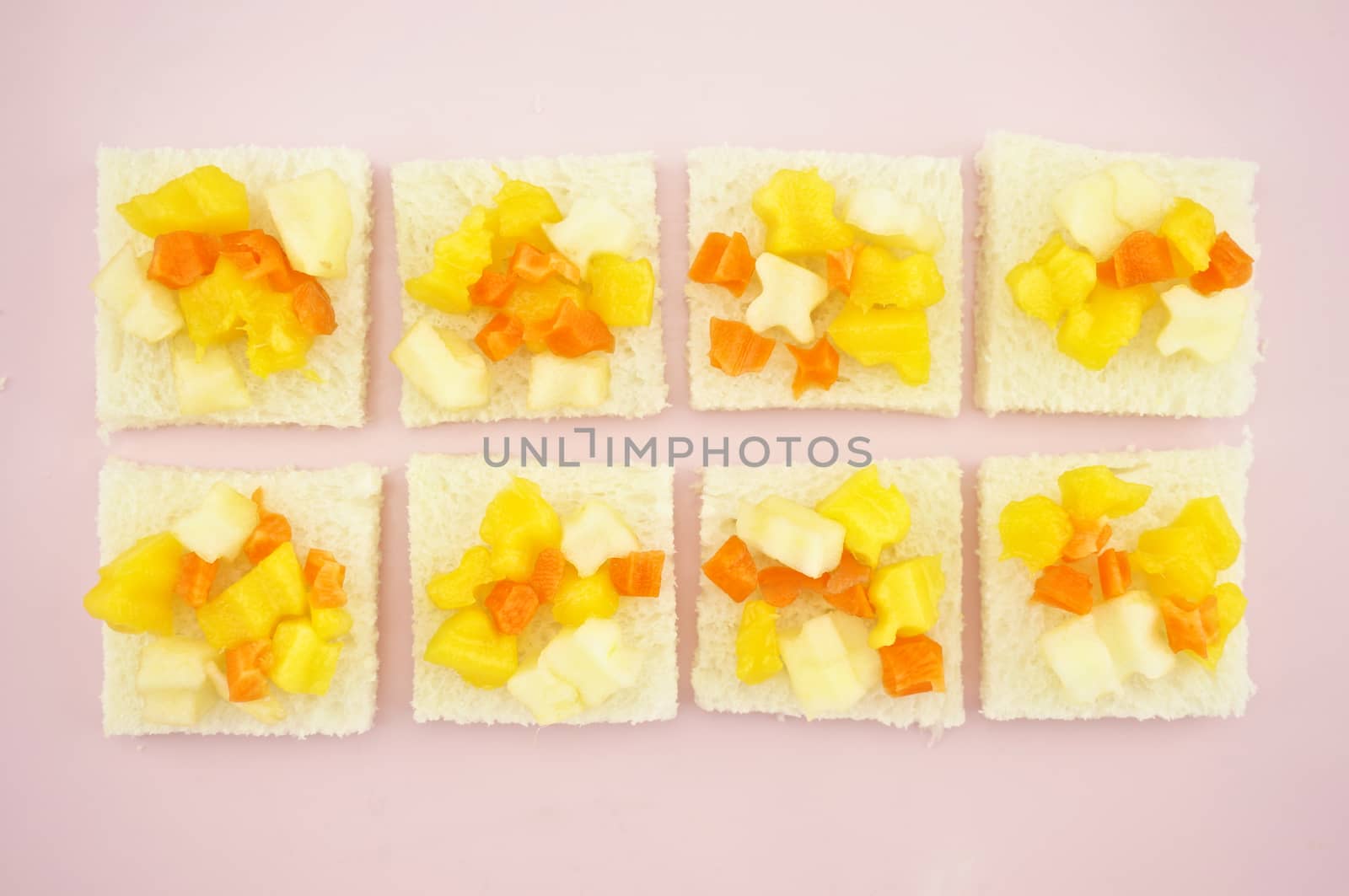 Carrot, Mango and apple sliced put on small bread in row on pink tray.