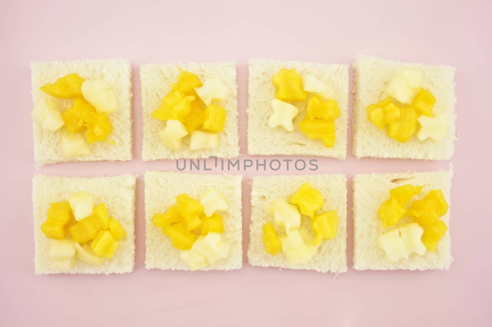 Mango and apple sliced put on small bread in row on pink tray.