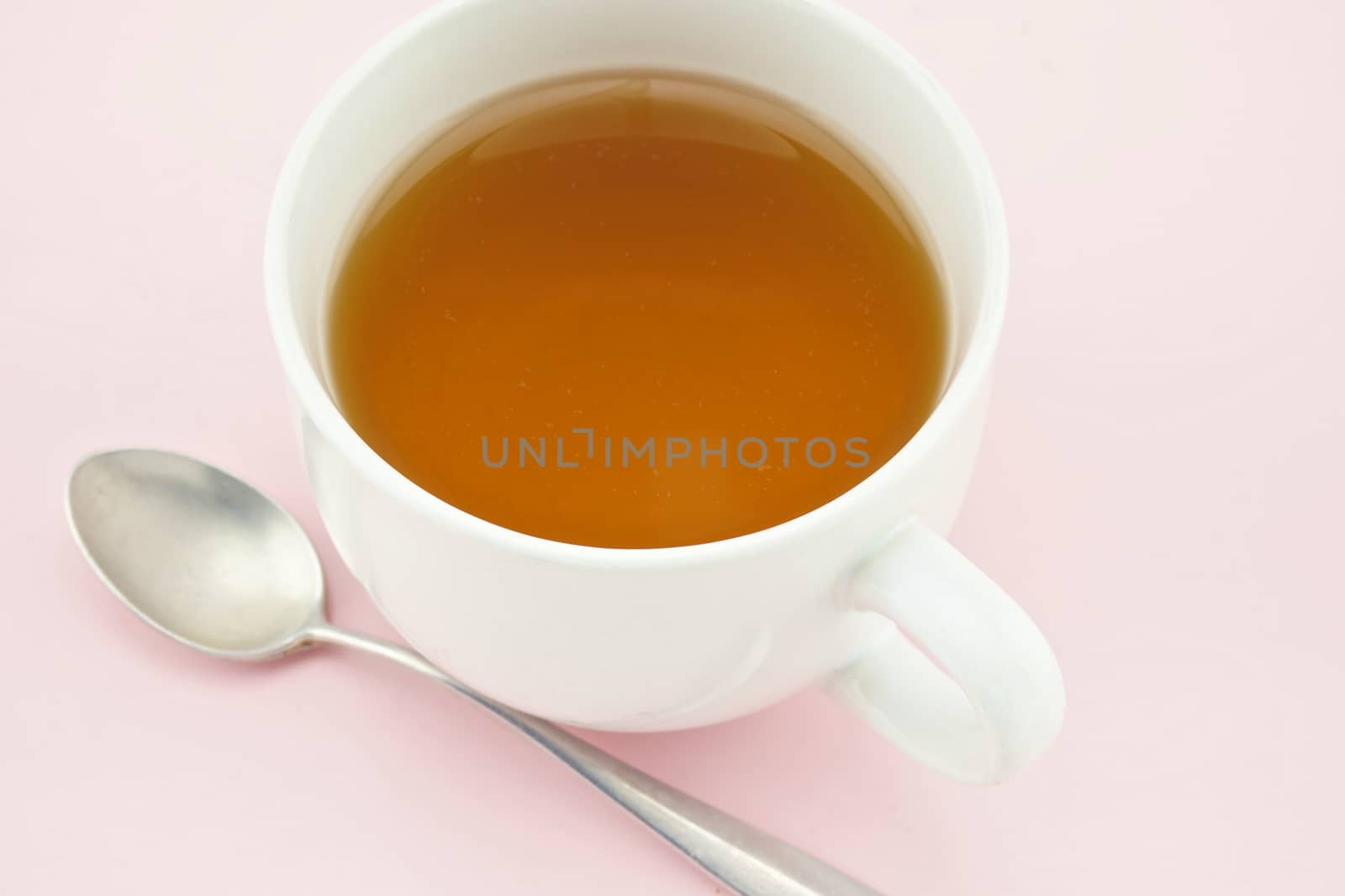 Tea in white cup and spoon at side put on pink tray.