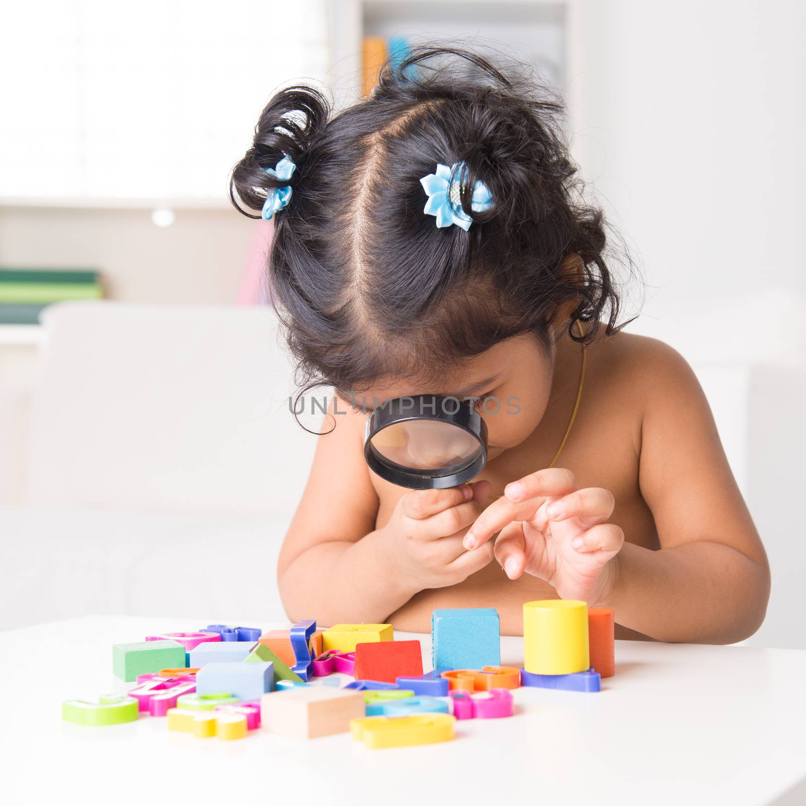 A little Indian girl zoom into toys through a magnifying glass, living lifestyle at home.