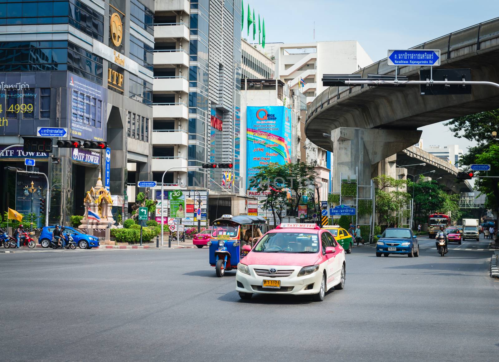 BANGKOK, THAILAND - 21 NOV 2013: Taxi and traditional tuk-tuk pass on crossroads street with skytrain track on background