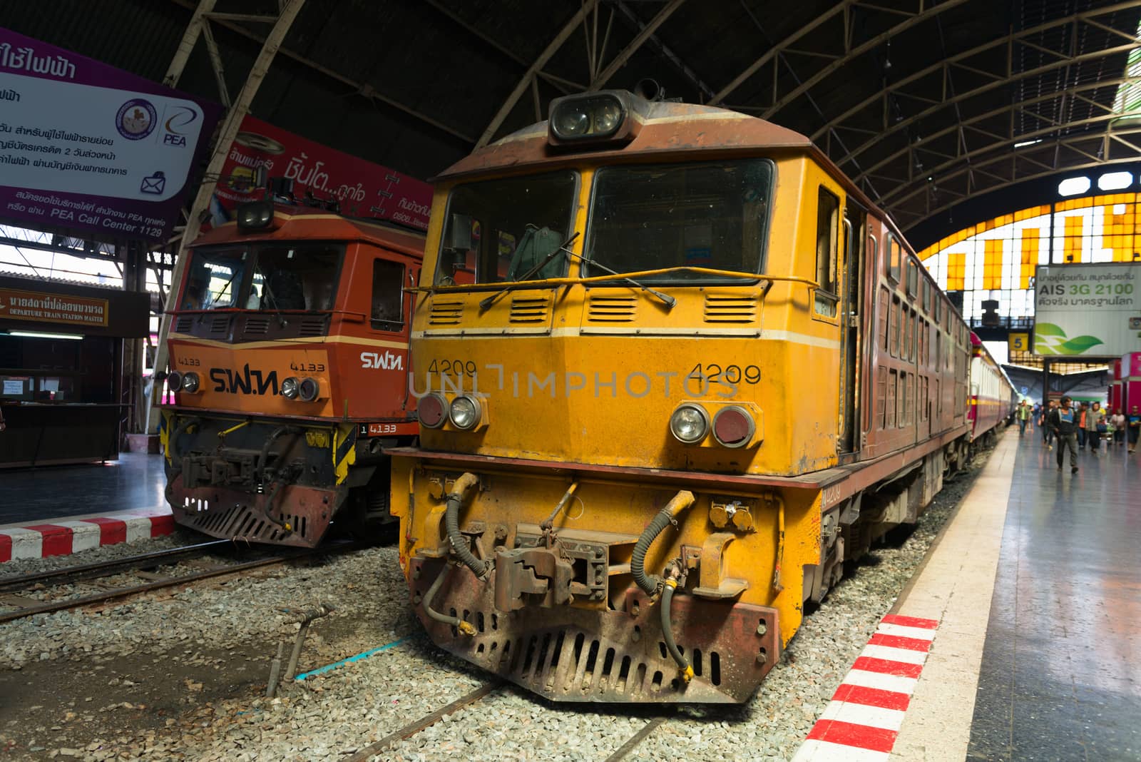 BANGKOK, THAILAND - 21 NOV 2013: Yellow locomotive and trains stand at central Krungthep Hua Lamphong railway station with people on platforms